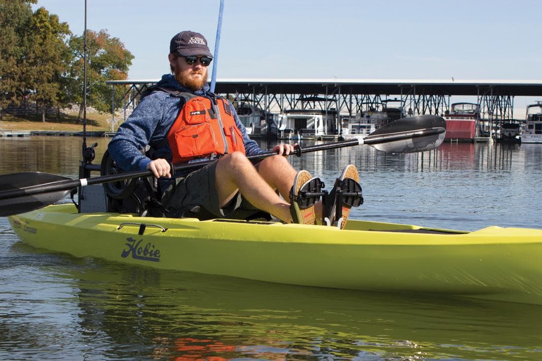 Man kayaking on a 2022 Hobie Compass in calm waters near a marina.
