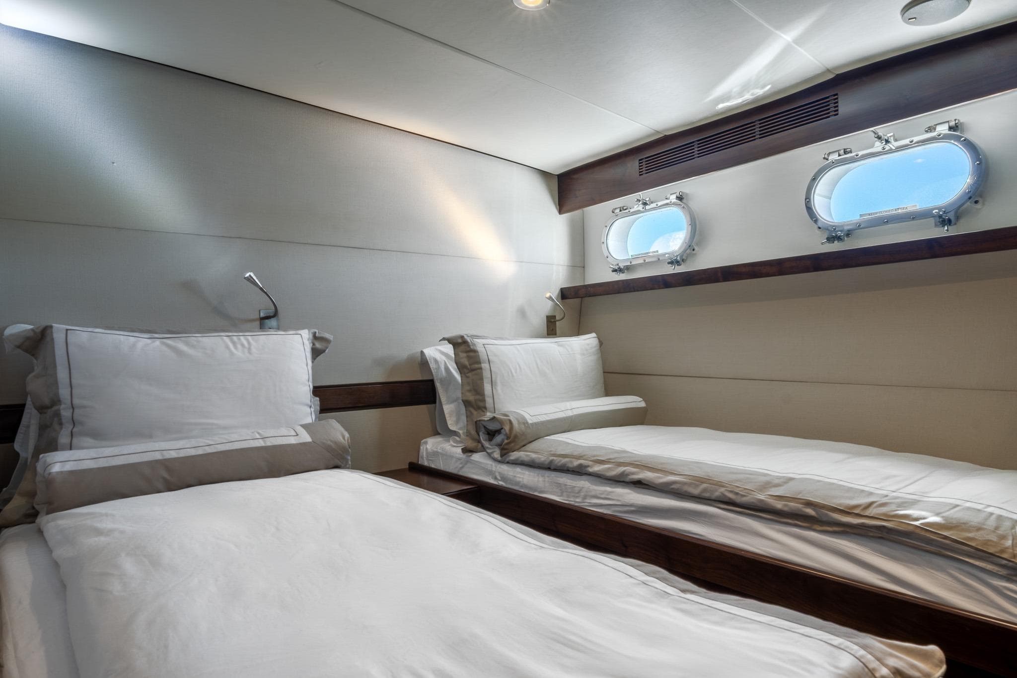 Luxurious twin cabin interior on a 1969 Feadship 25.8m yacht, featuring elegant bedding and porthole windows.