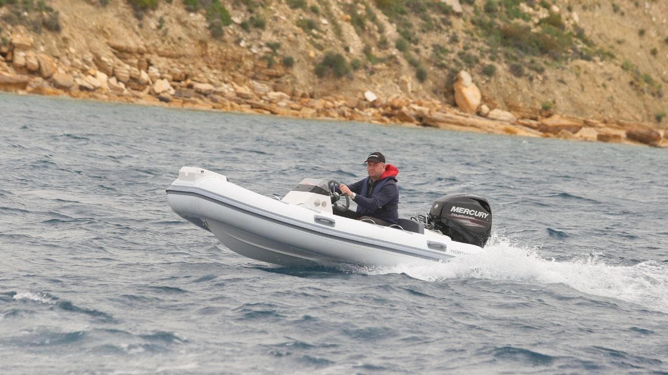 2022 Northstar Axis 3.4 inflatable boat cruising on open water near rocky shoreline.
