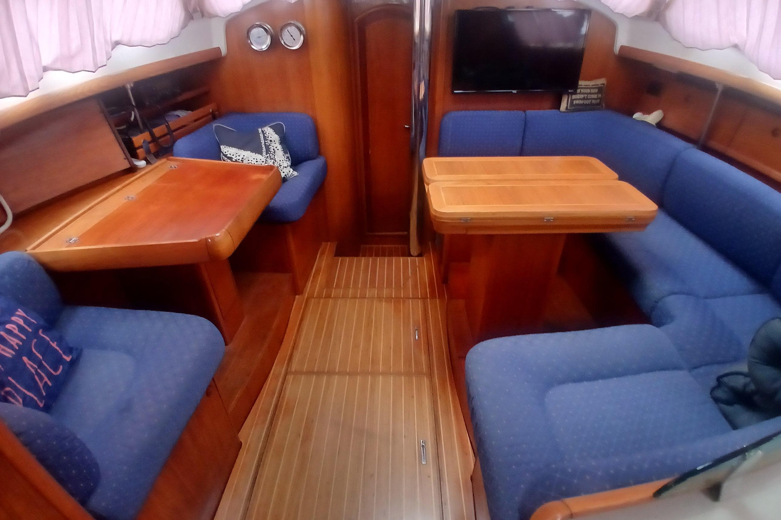 Interior of 2002 Jeanneau Sun Odyssey 43 DS yacht with blue seating and wooden tables.