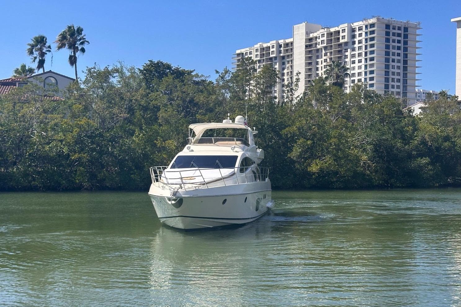 2007 Azimut 55E yacht cruising on a calm river with lush greenery and buildings in the background.