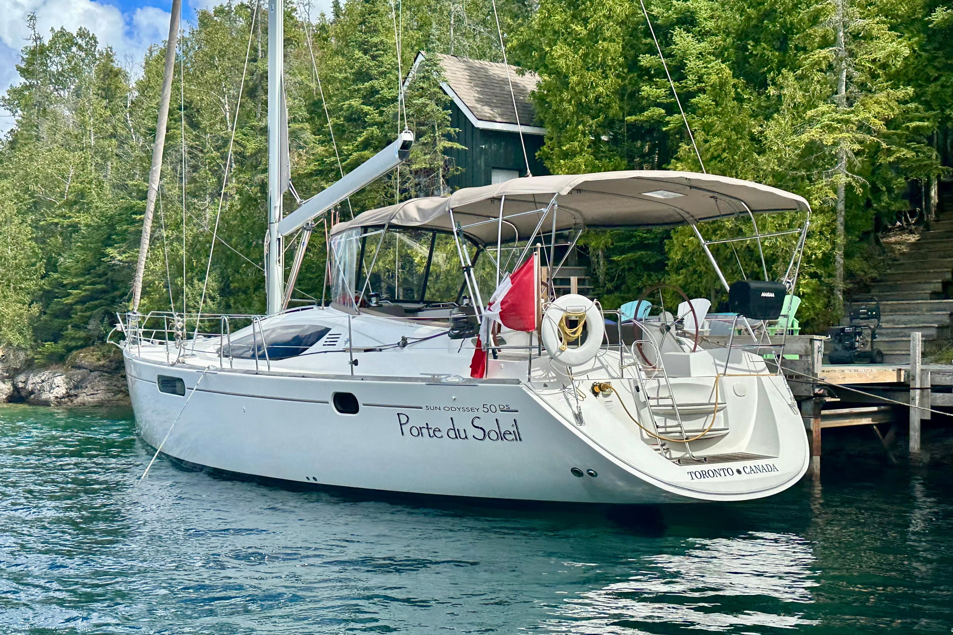 2015 Jeanneau Sun Odyssey 50 DS sailboat docked by lush greenery.