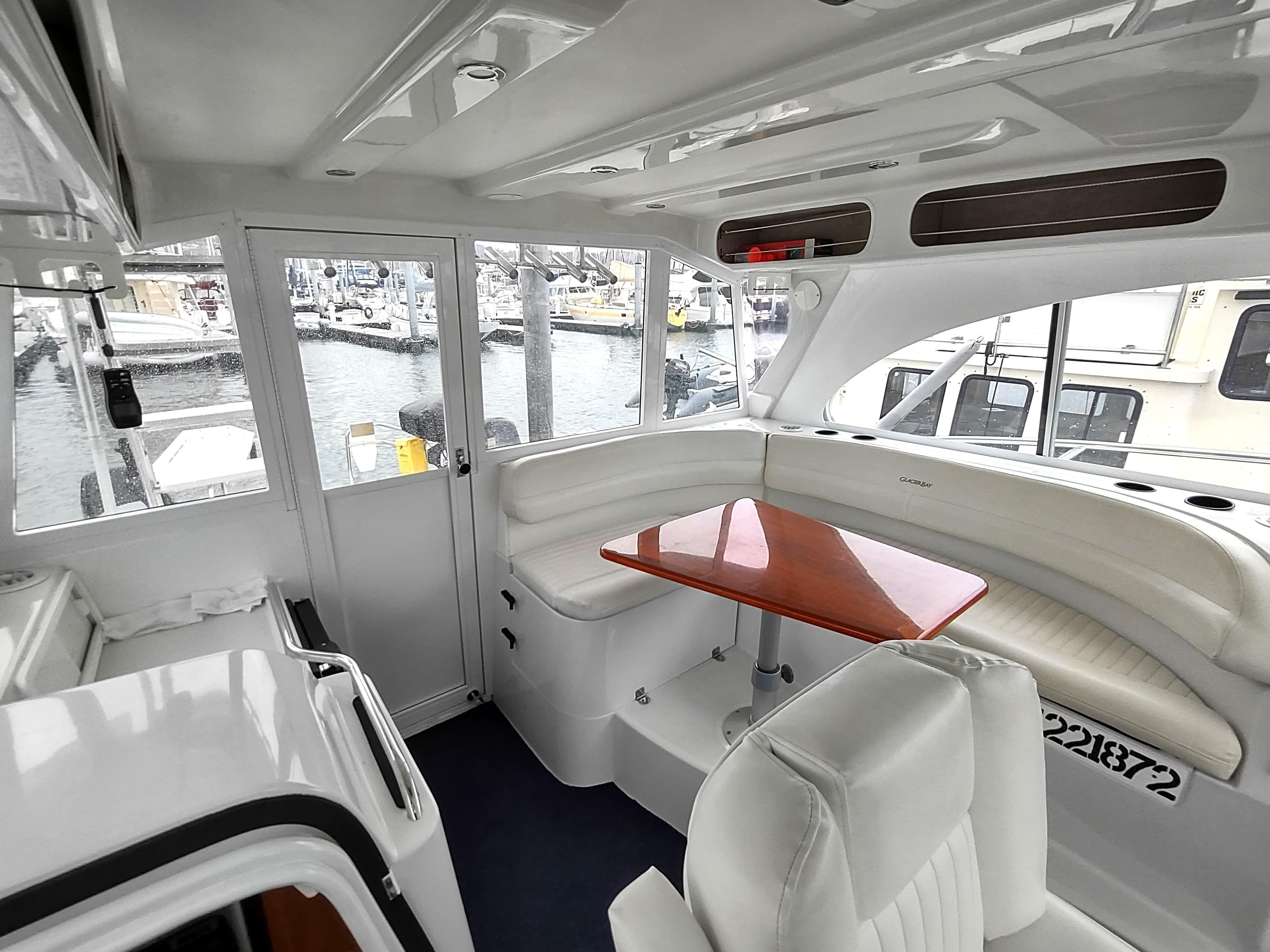 Interior of 2005 Glacier Bay 3490 Ocean Runner with white seating and wooden table.