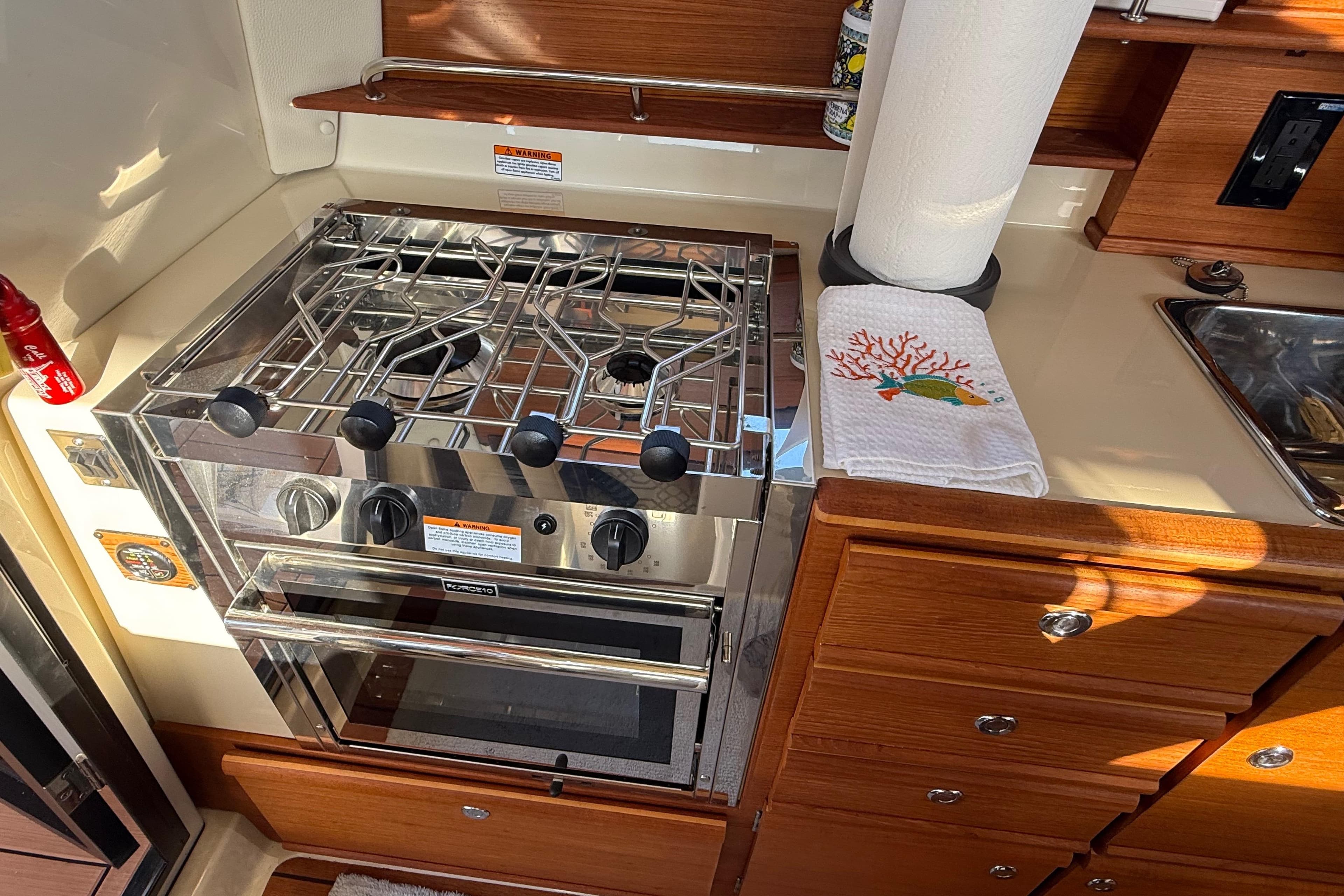 2022 Ranger Tugs R-27 kitchen with stainless steel stove and wooden cabinetry.