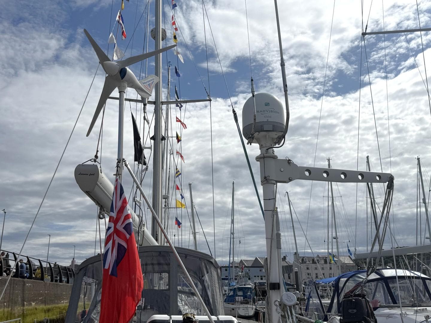 Najad 490 sailboat from 2002 with flags and wind turbine at a marina.
