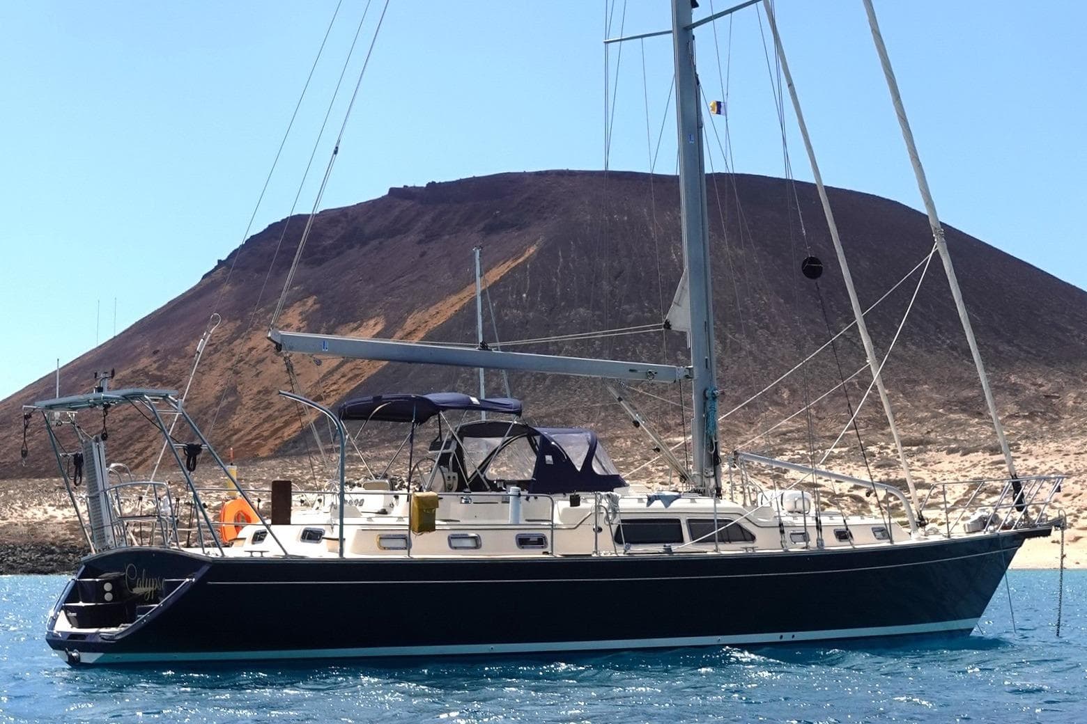 2006 Island Packet 485 sailboat anchored near a volcanic island, clear blue sky.