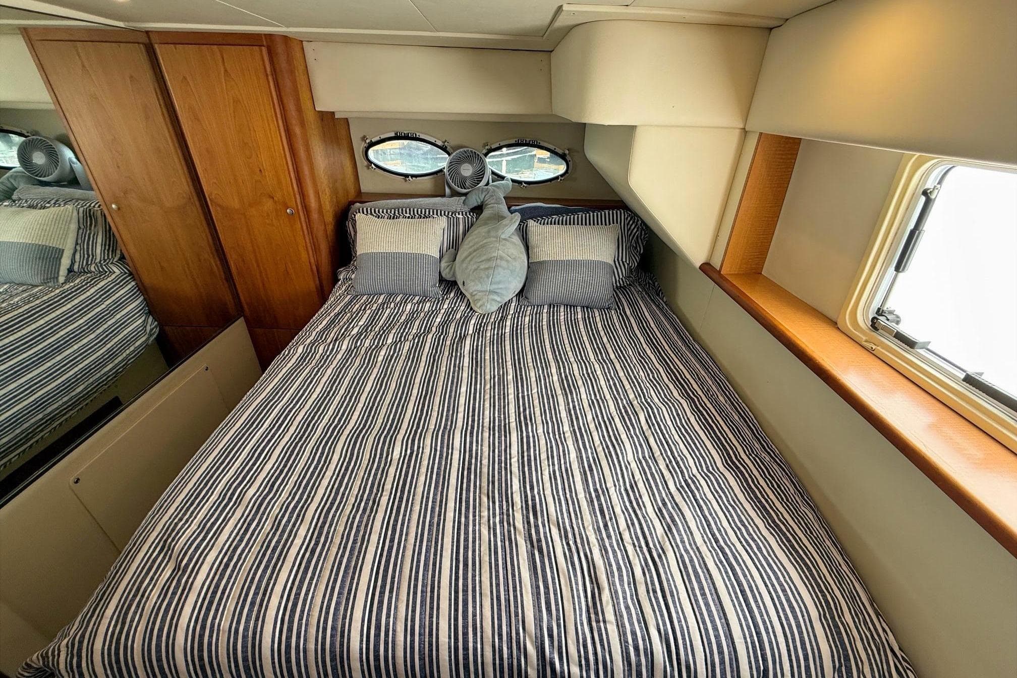 Interior of 1999 Silverton 392 Motor Yacht with striped bedding and wooden cabinetry.
