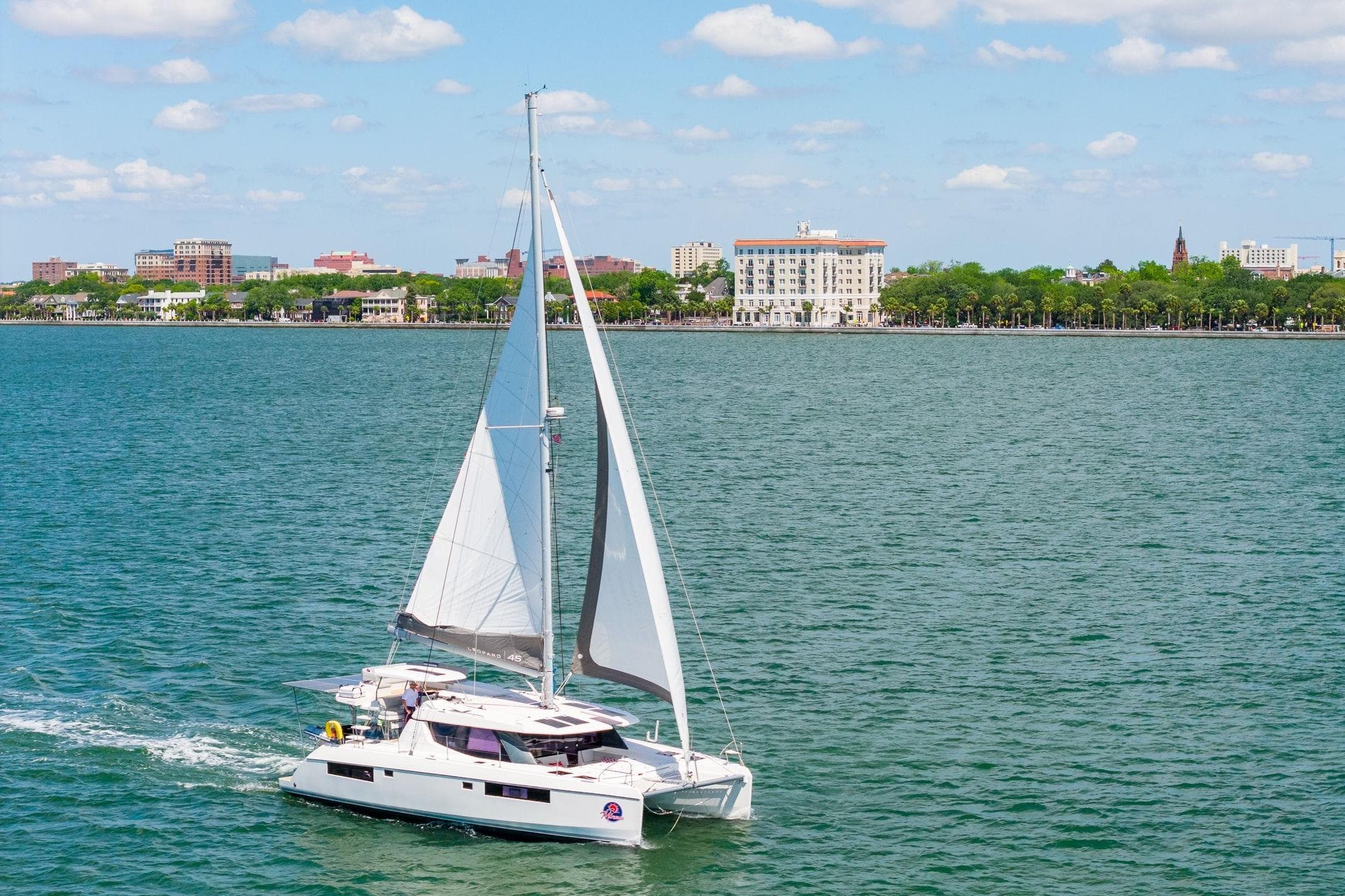 Sailing catamaran Leopard 45, 2020 model, cruising near a coastal city skyline.