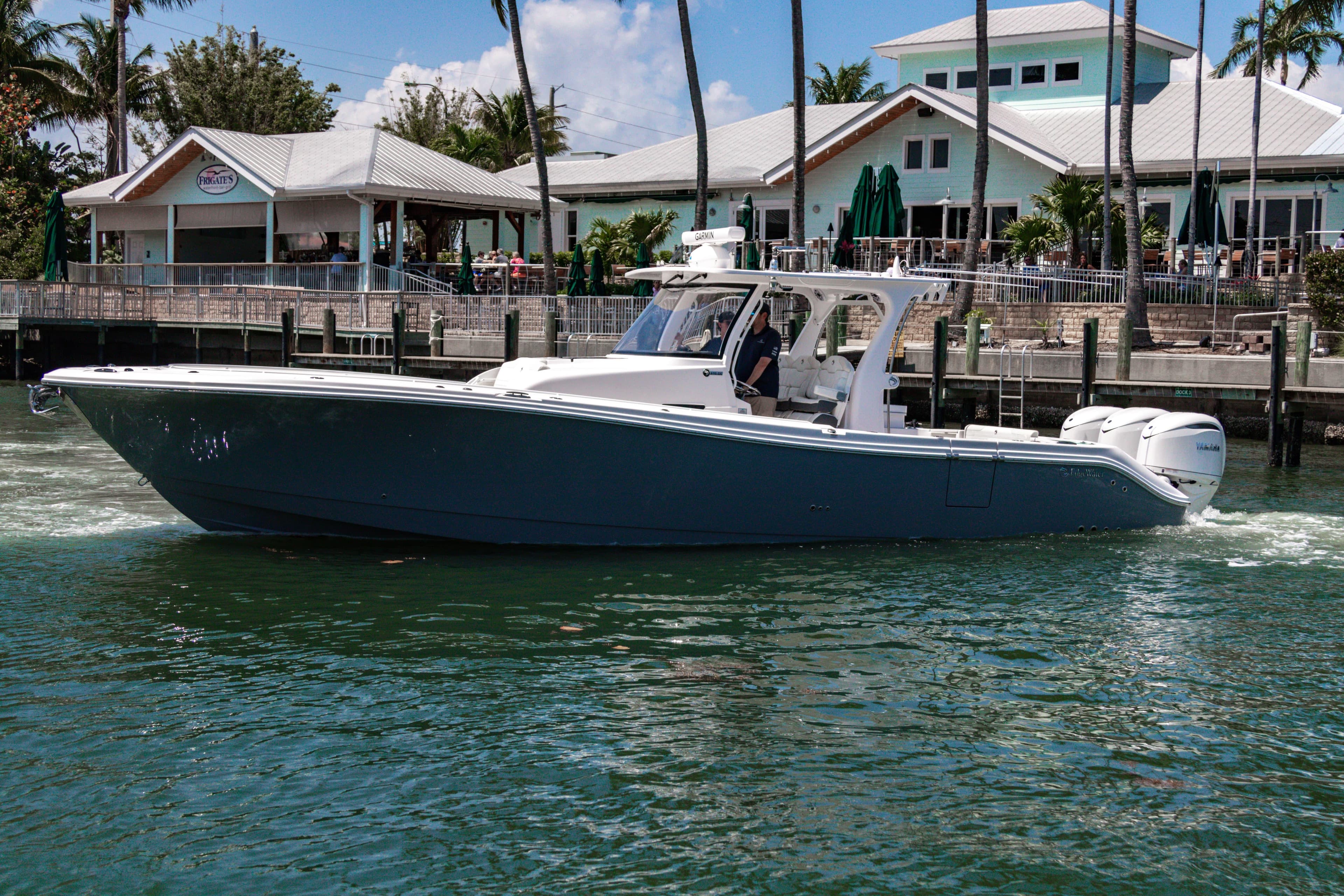 2025 Edgewater 370CC boat cruising near a waterfront restaurant with palm trees.