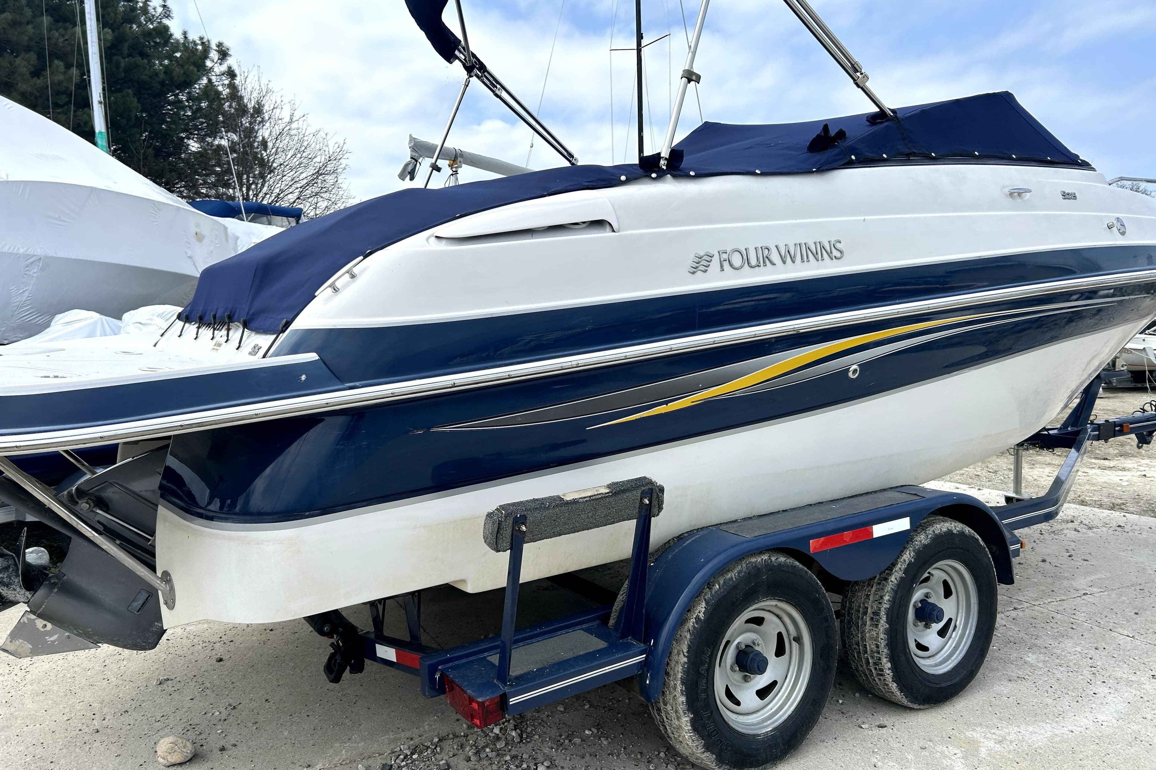2009 Four Winns S215 boat on trailer, blue and white design, parked outdoors.