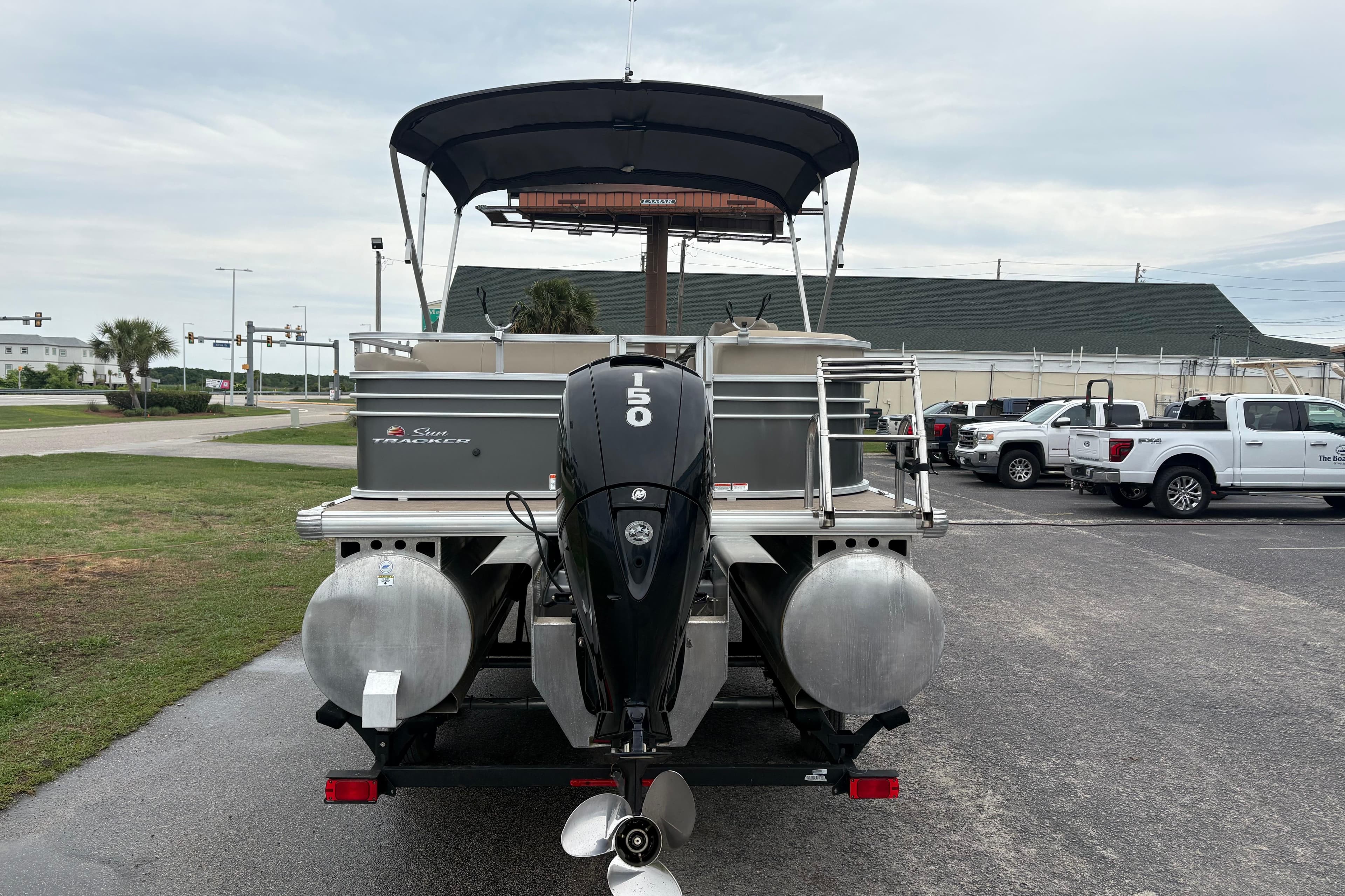2023 Sun Tracker Party Barge 22 DLX pontoon boat with 150 HP engine, parked outdoors.
