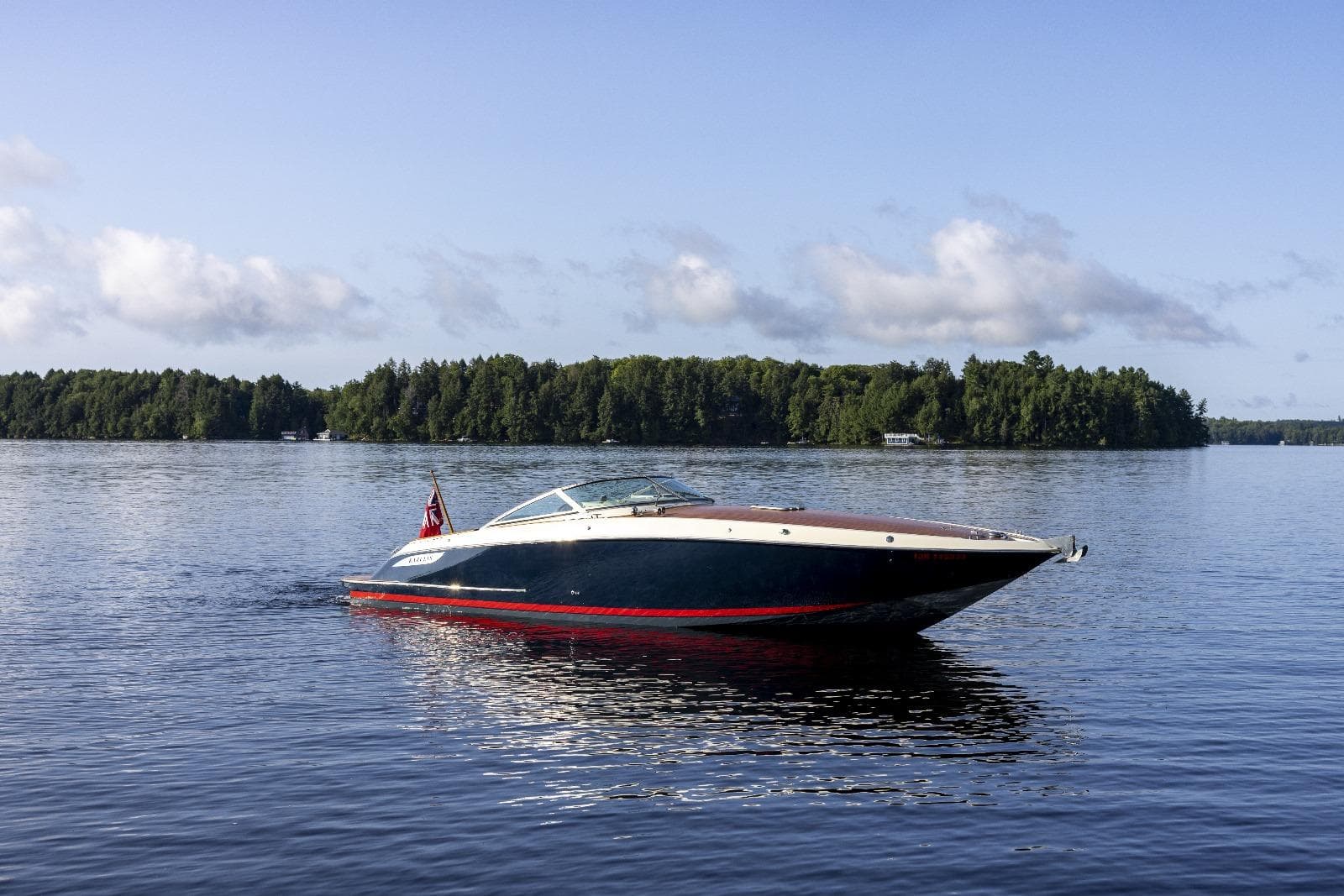 Kavalk 30 boat from 1997 cruising on a serene lake with forested shoreline.