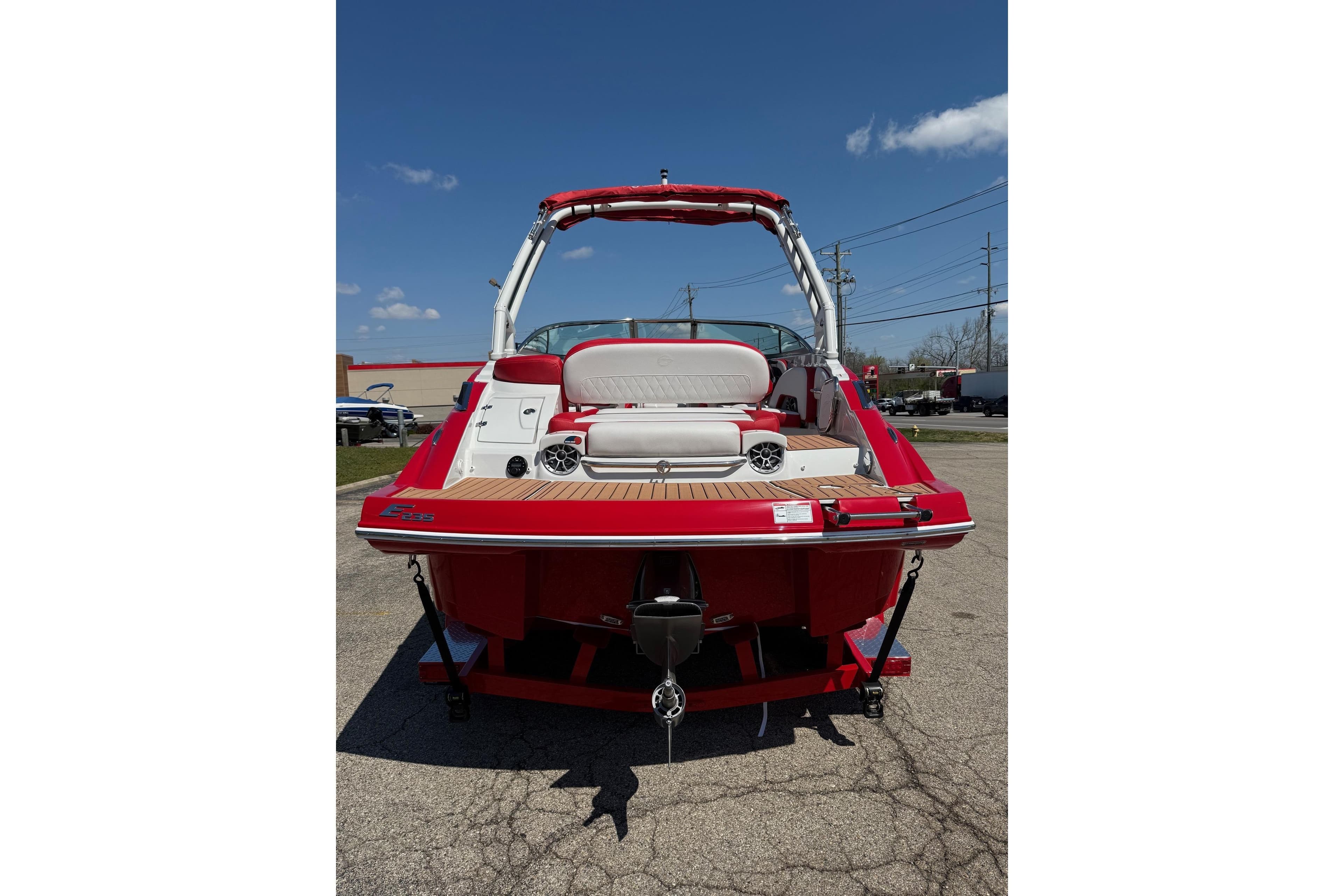 Red 2025 Crownline Eclipse E235 boat, rear view, parked on pavement under clear blue sky.