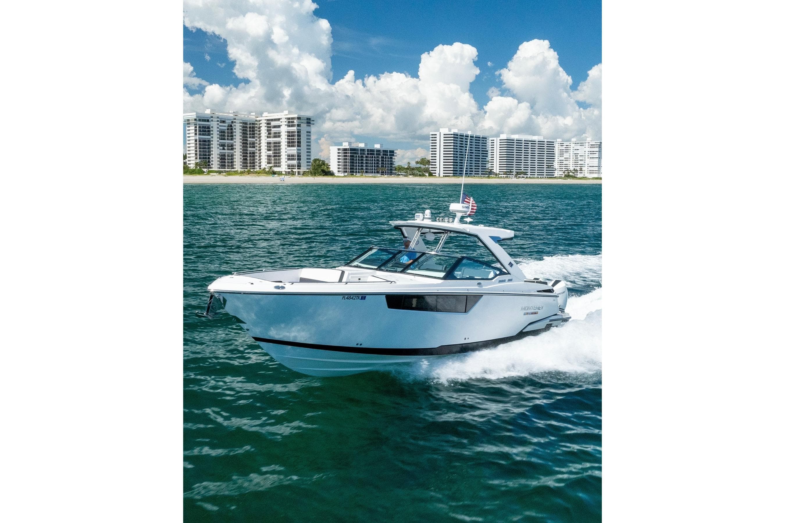 2026 Monterey 385SS Super Sport cruising on ocean near modern beachfront buildings.