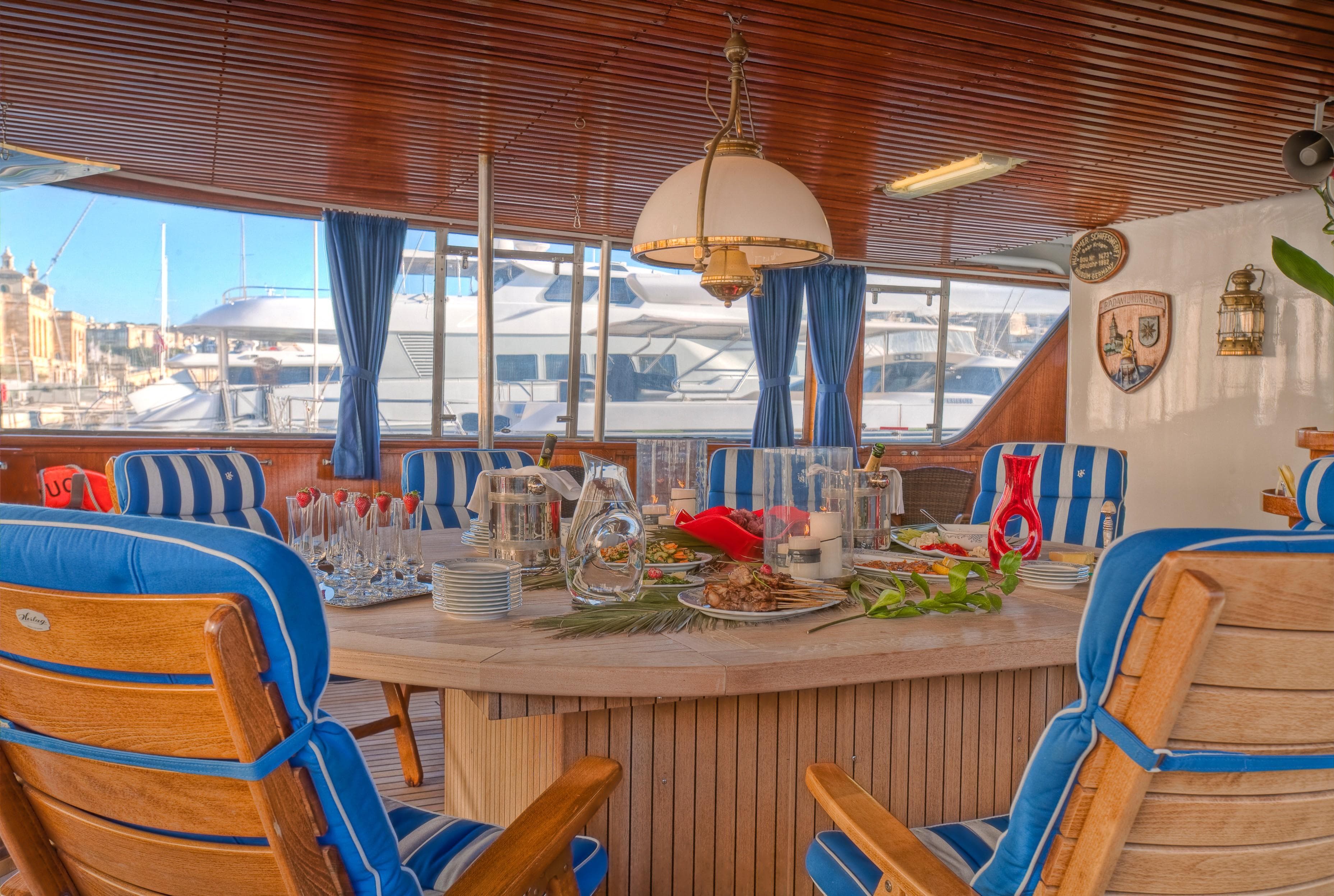 Luxurious yacht dining area with blue-striped chairs, elegant table setting, and marina view.