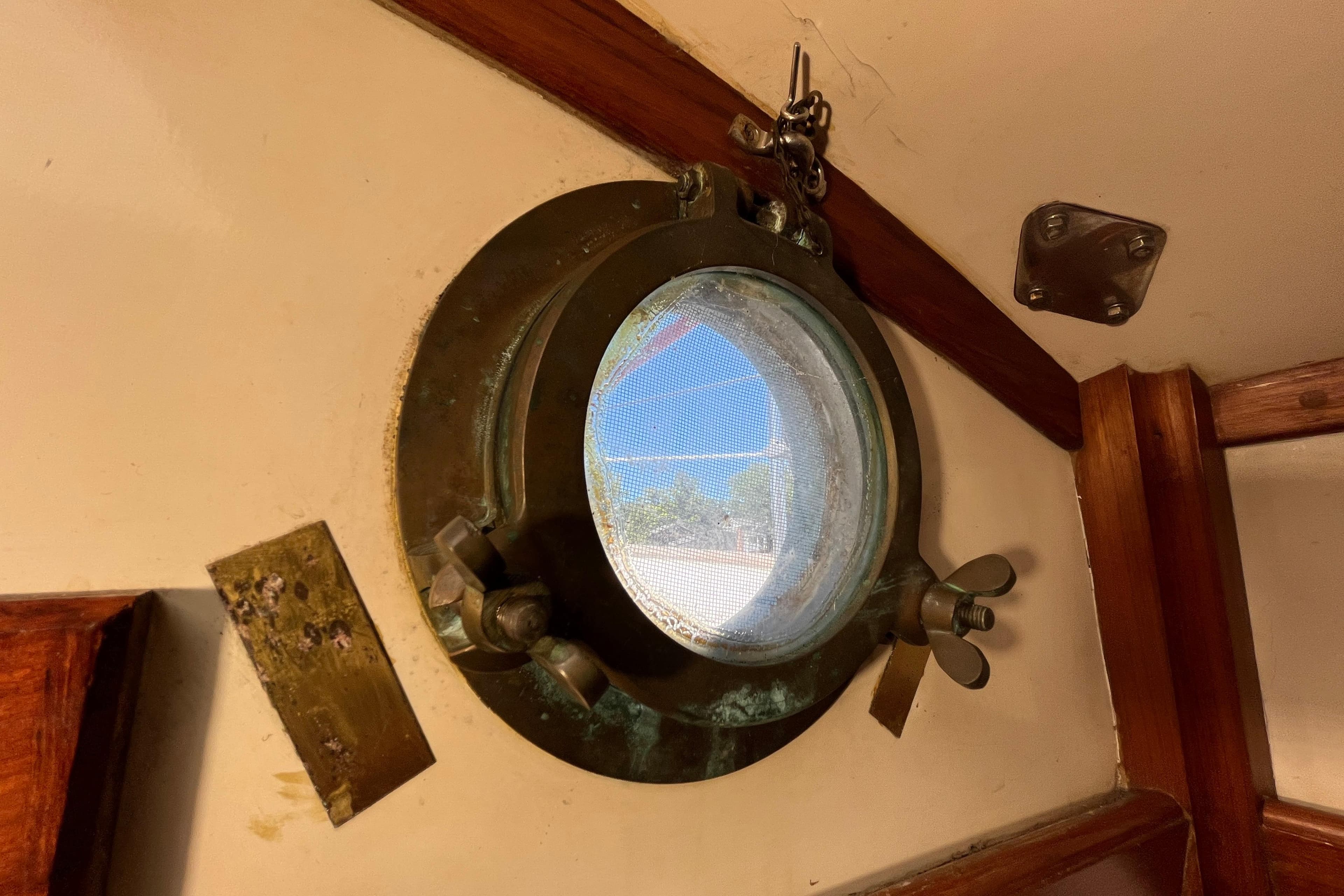 Circular porthole on 1982 Tayana 37 sailboat, featuring brass fittings and wooden trim.