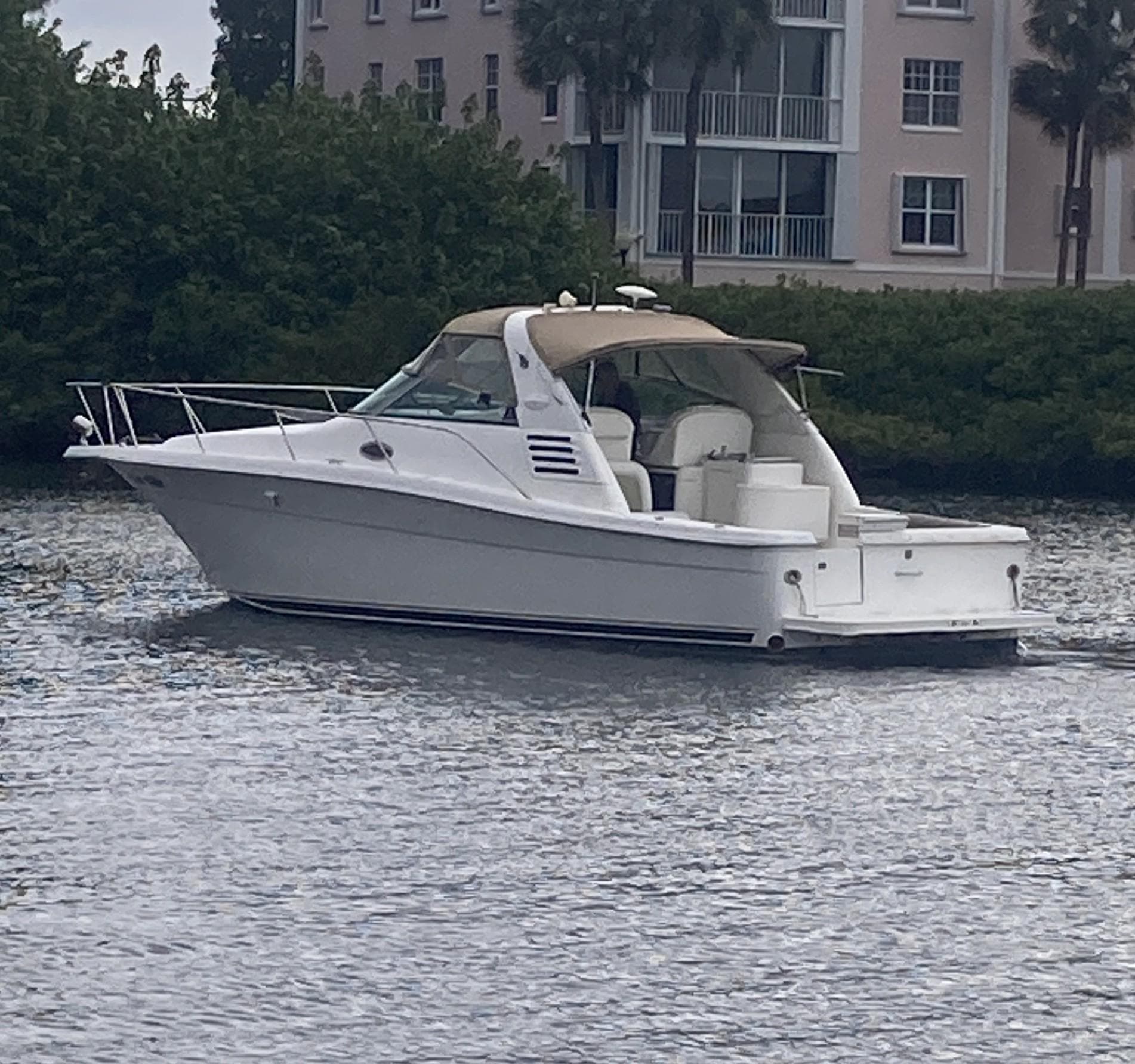 1999 Sea Ray 330 Express Cruiser on calm water near buildings and greenery.