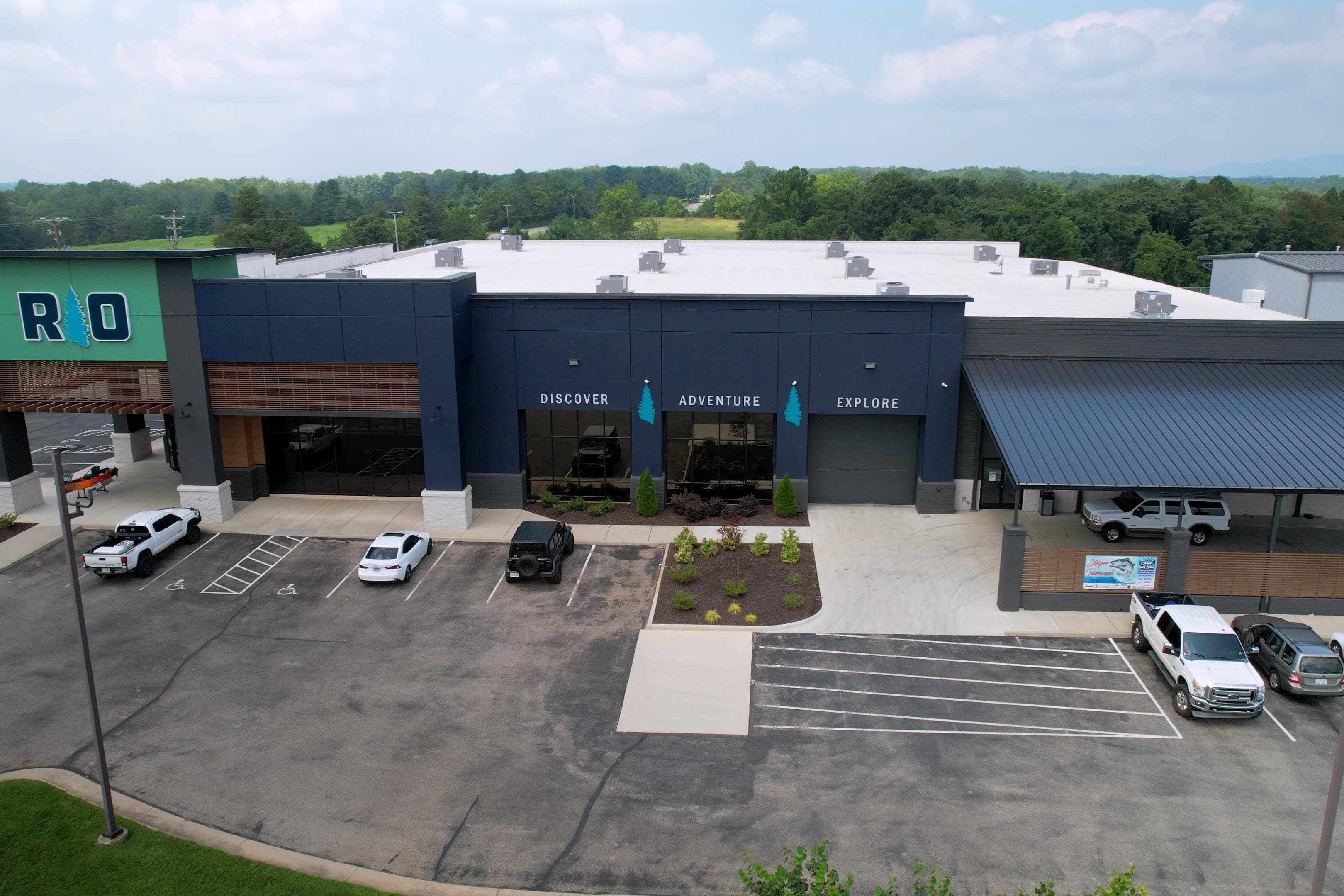 Aerial view of a modern building with parking, featuring "Discover Adventure Explore" signage.