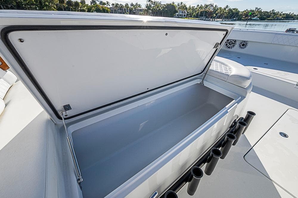 Open storage compartment on 2023 Freeman 47 boat, featuring rod holders and scenic waterfront view.