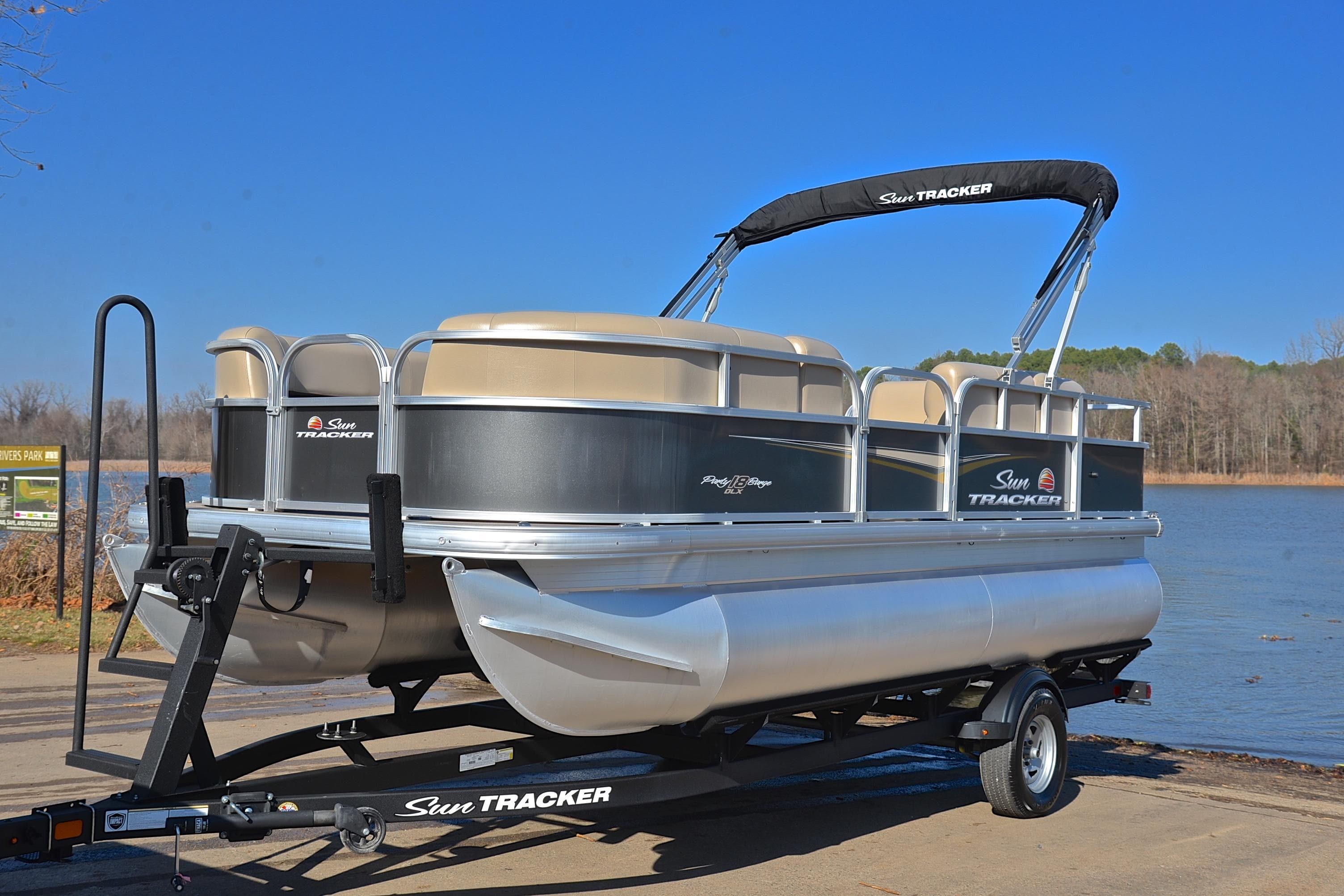 2025 Sun Tracker Party Barge 18 DLX pontoon boat on trailer by a lake.
