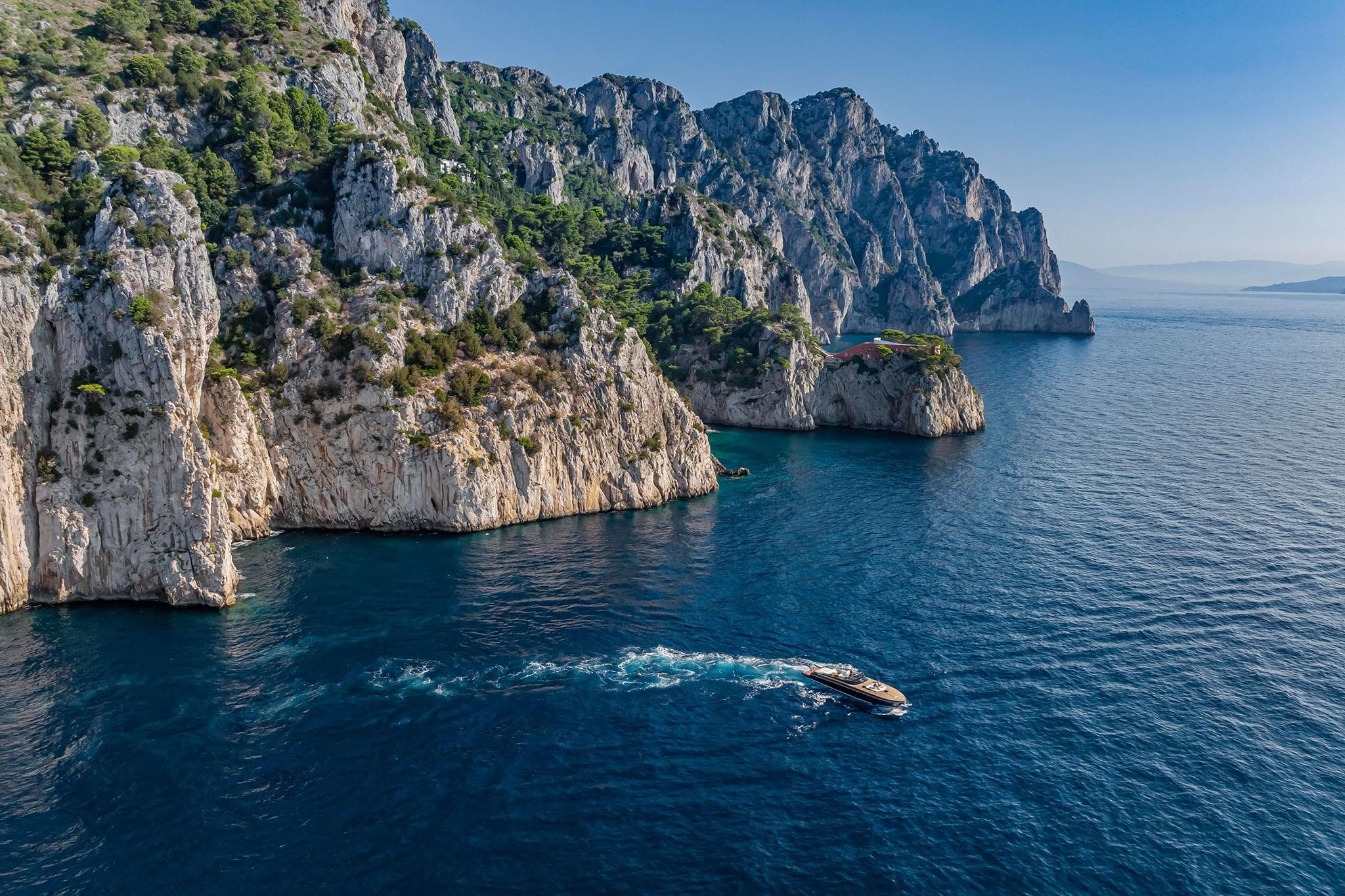 Luxury Itama 62 RS yacht cruising near stunning rocky cliffs, 2024 model.
