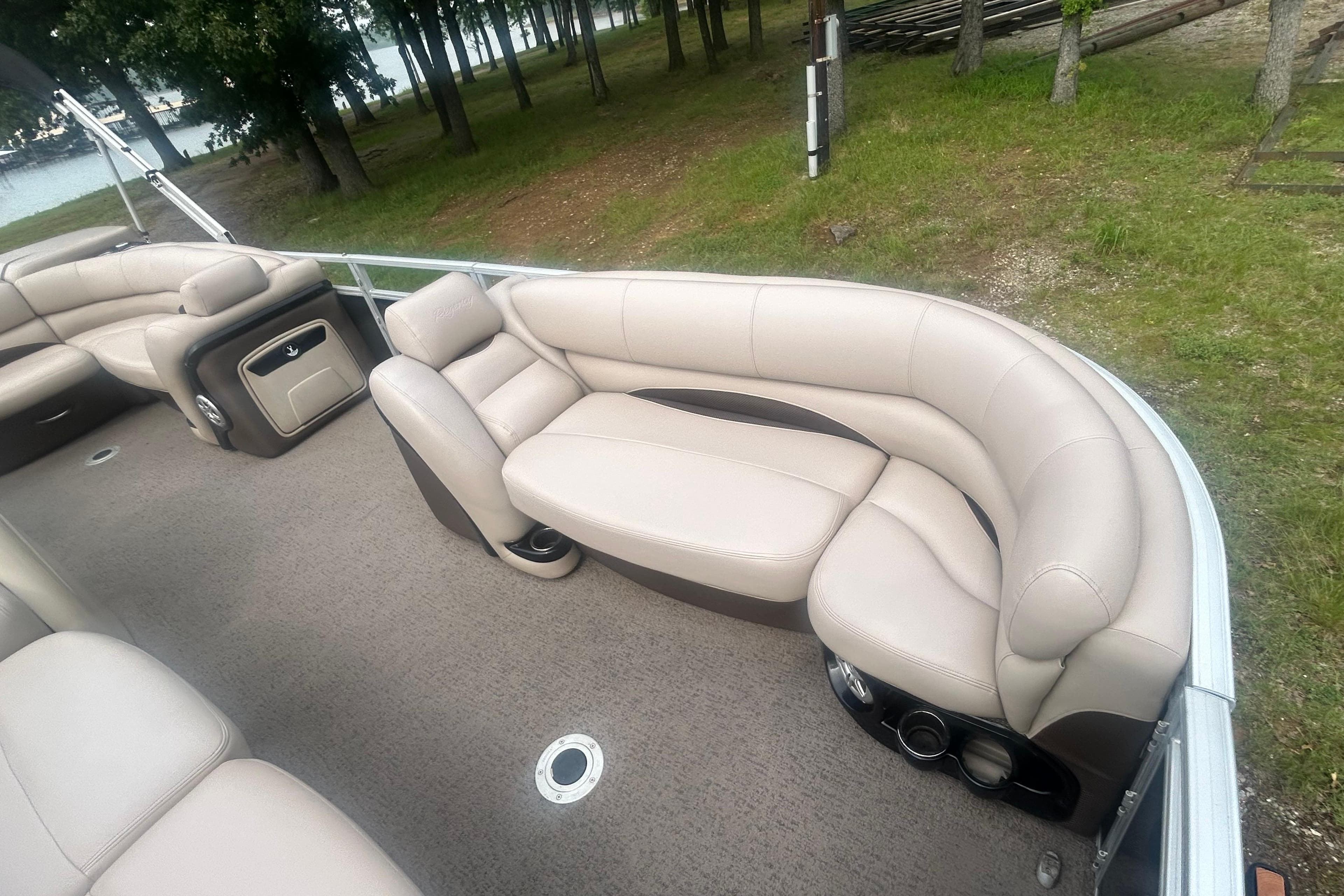2014 Regency 220 DL3 pontoon boat with beige seating, docked near a wooded shoreline.