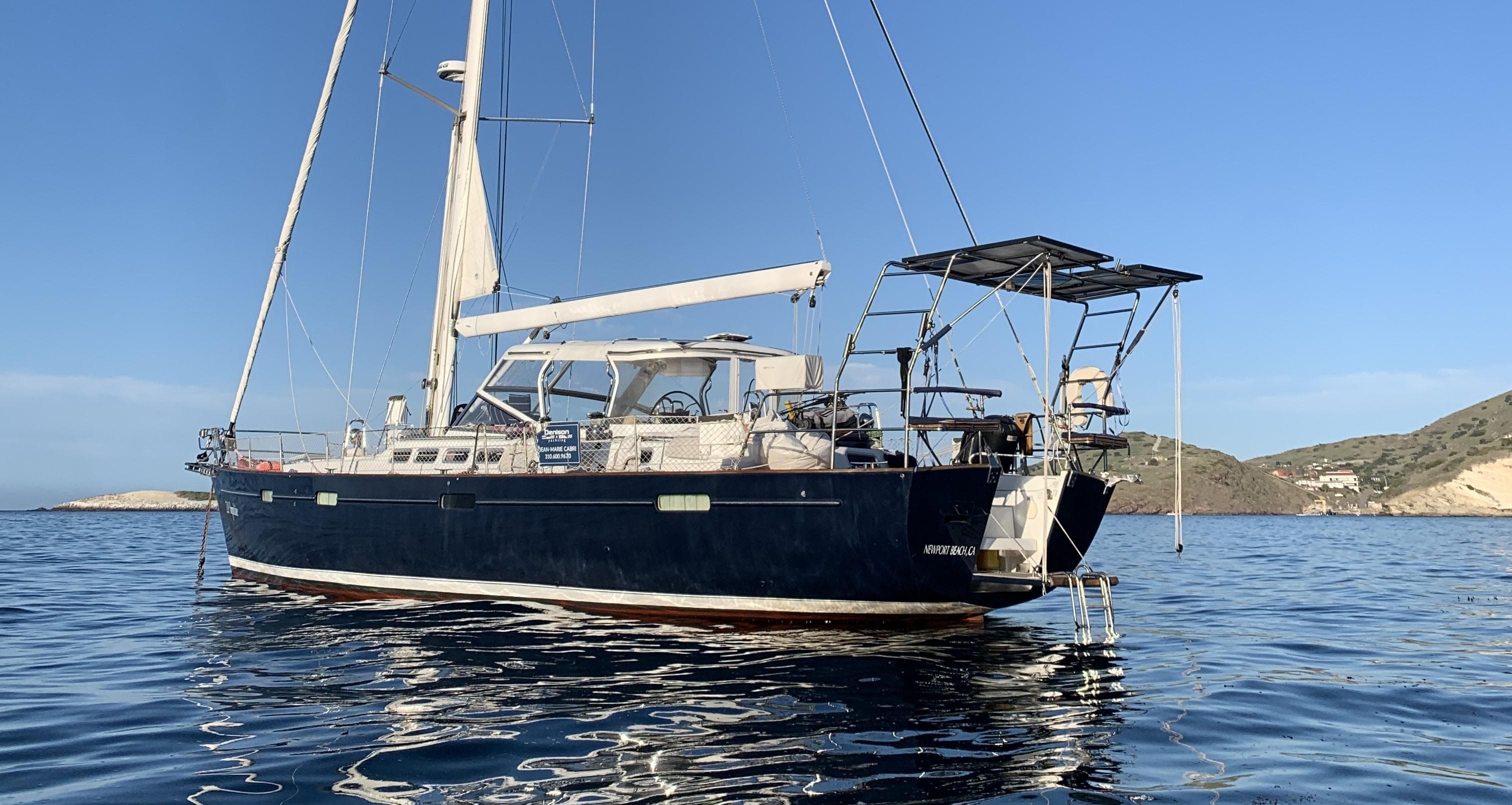 2005 Beneteau 57 sailboat anchored in calm waters, clear sky, coastal background.
