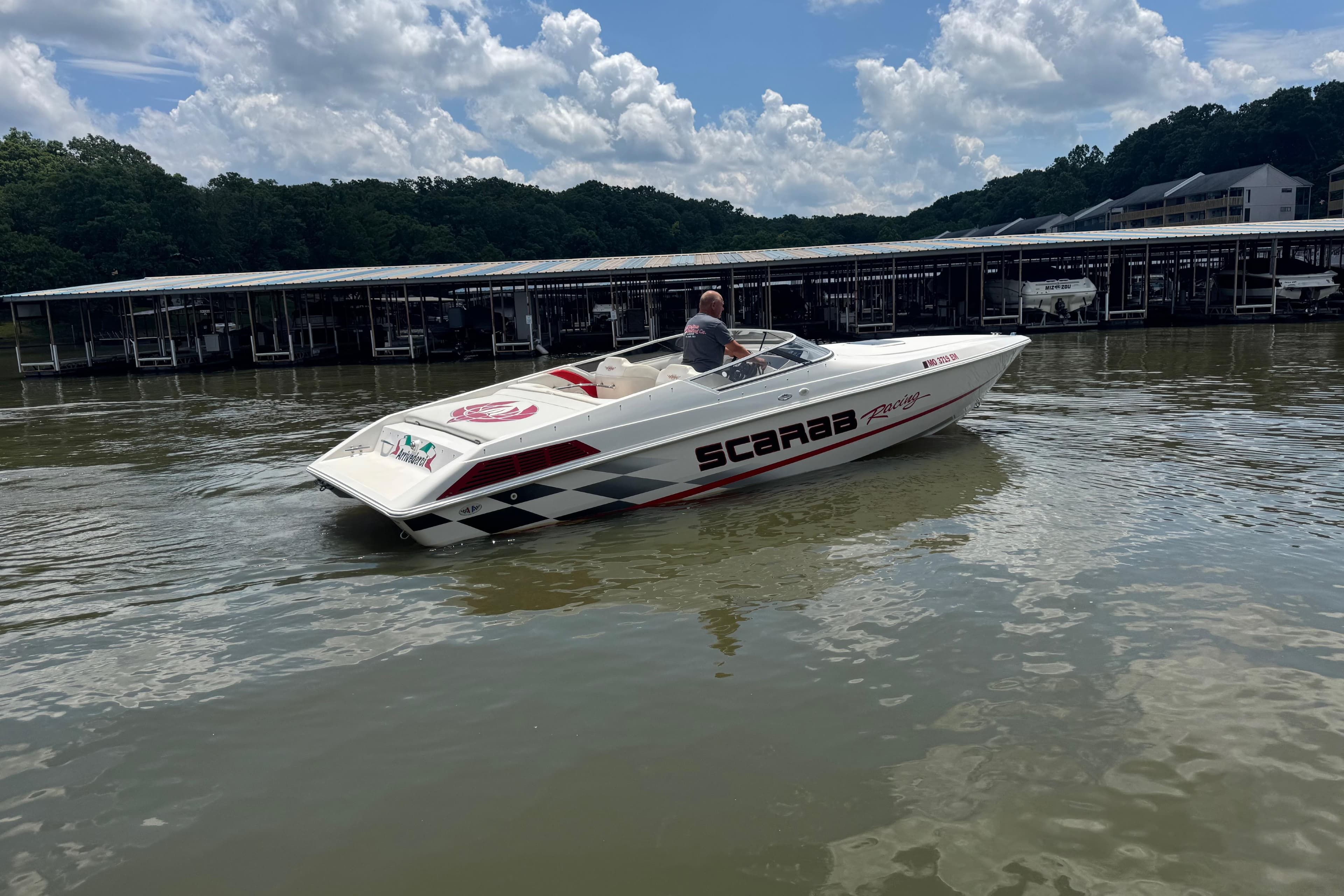 1997 Wellcraft 29 Scarab boat cruising on a lake near a marina.