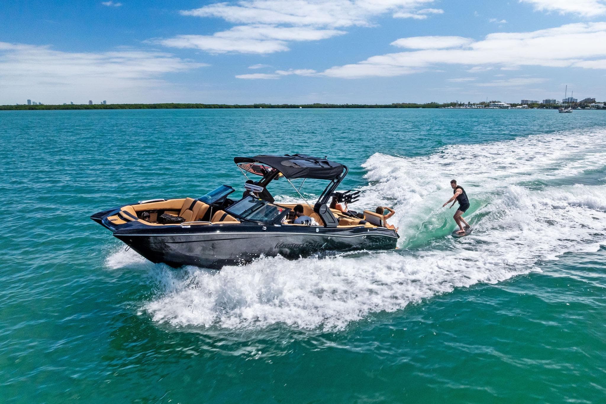 2024 MasterCraft X24 boat with wakeboarder on turquoise water under blue sky.
