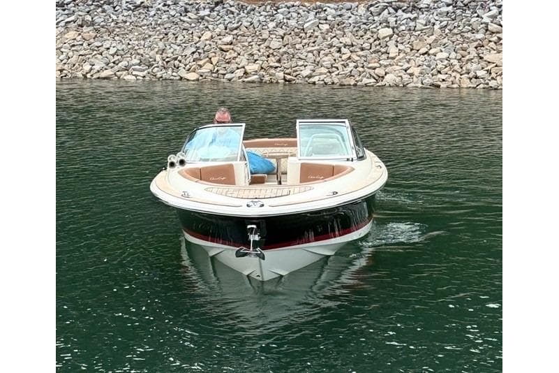 2017 Chris-Craft Launch 25 boat on calm water near rocky shoreline.