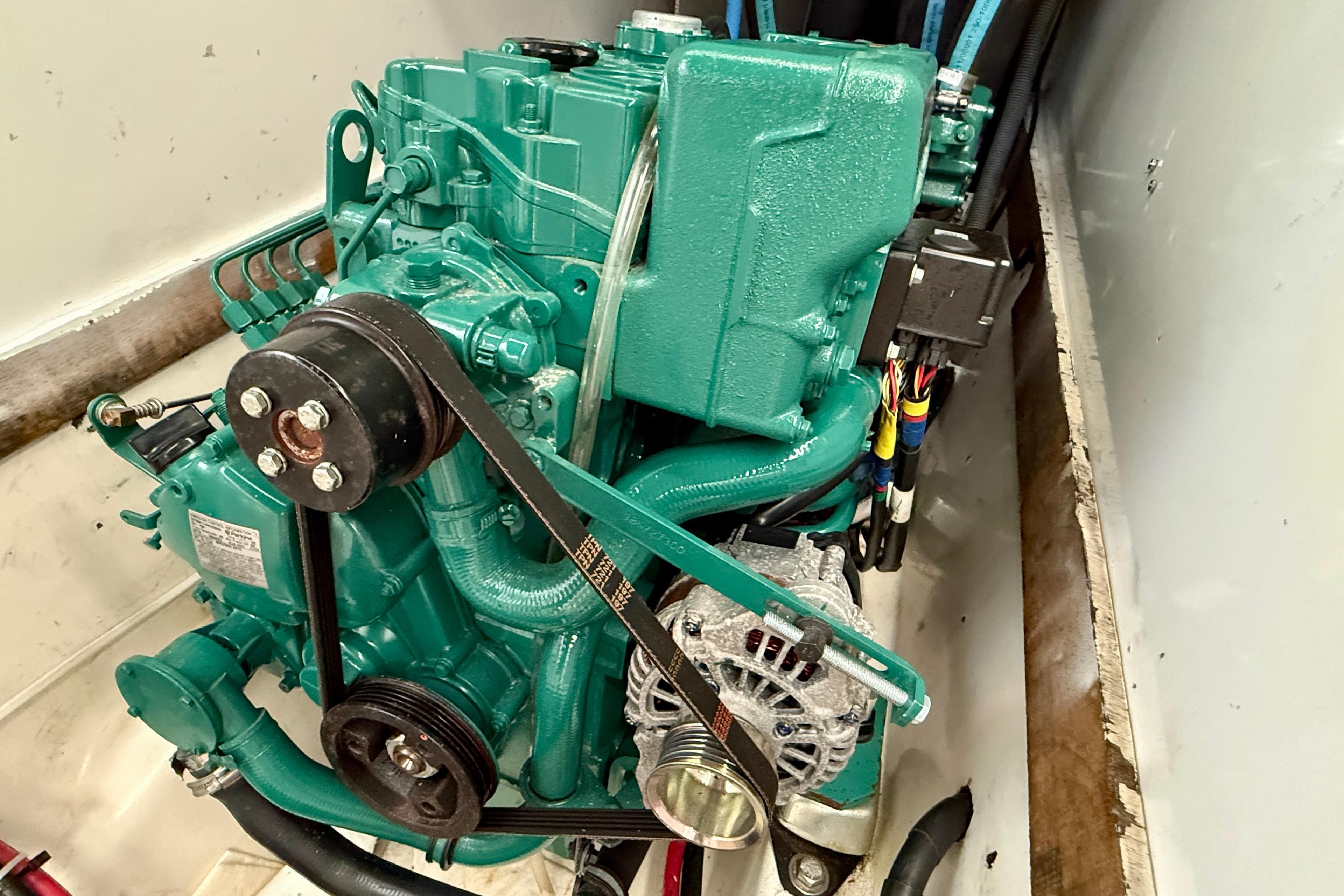 Engine of a 1985 MacGregor 65 sailboat, featuring a green motor and belt system.