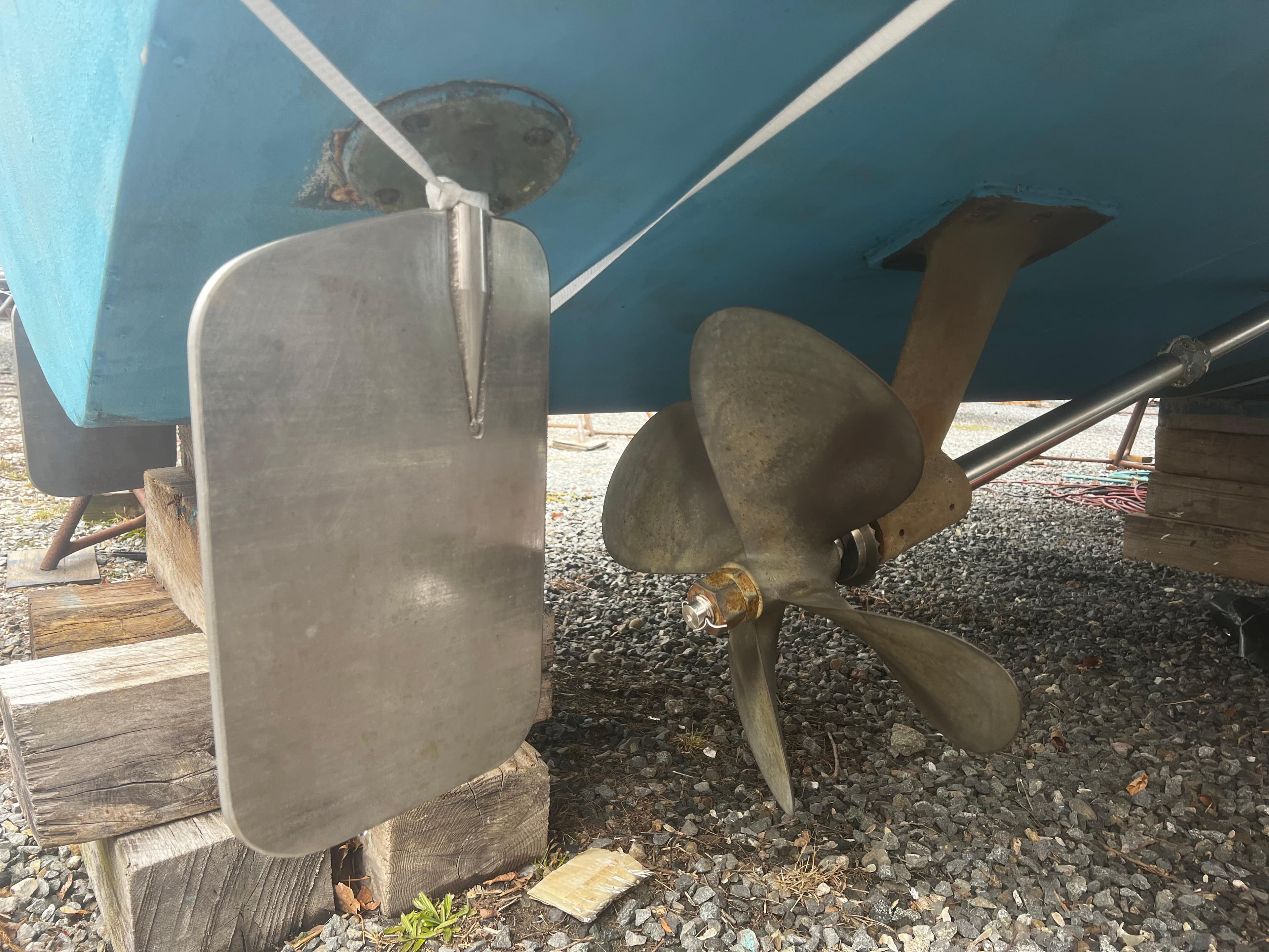 1975 Bertram 31 boat propeller and rudder on gravel, showcasing marine engineering.