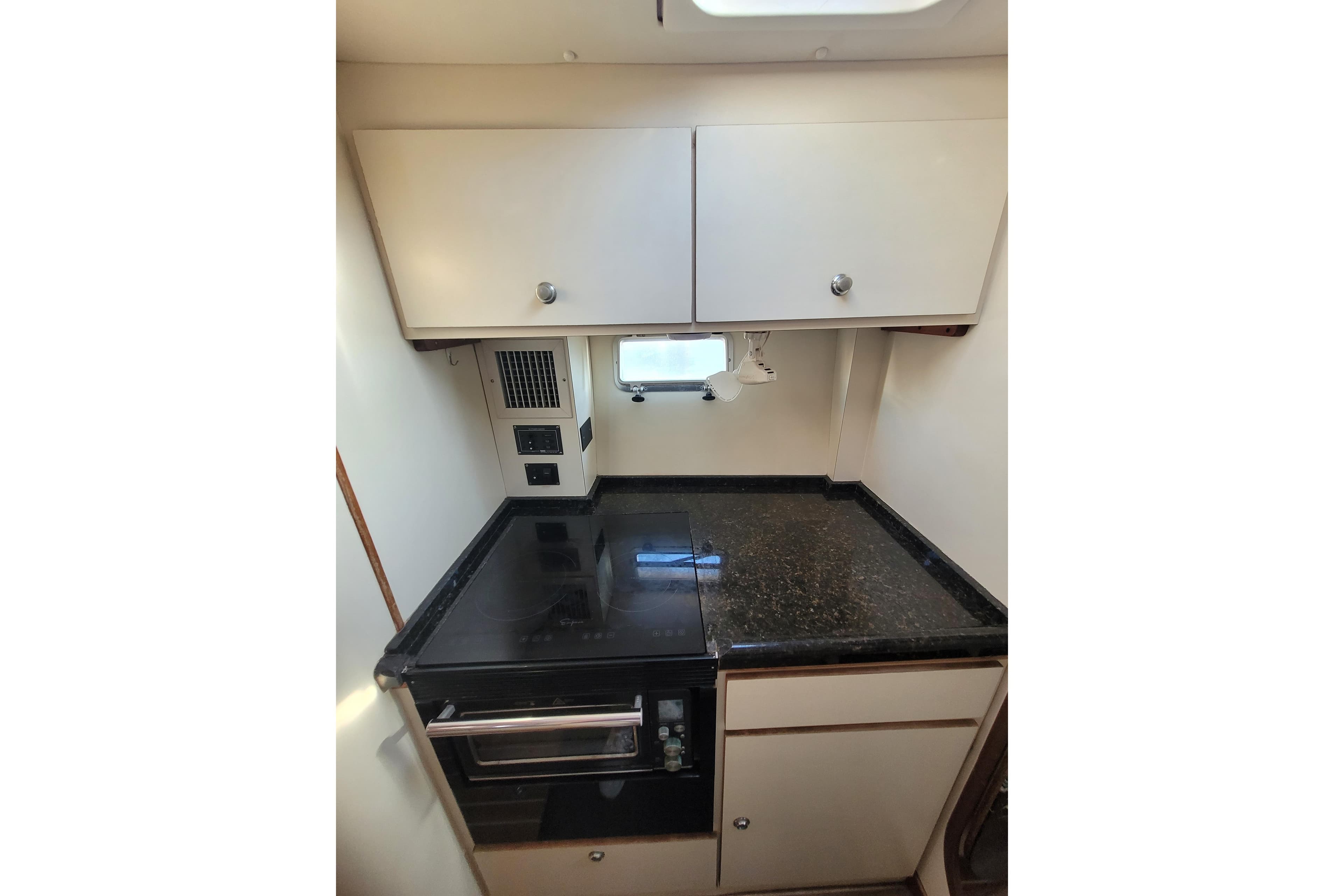 Compact kitchen area in a 1995 Lagoon TPI boat with black countertop and white cabinets.