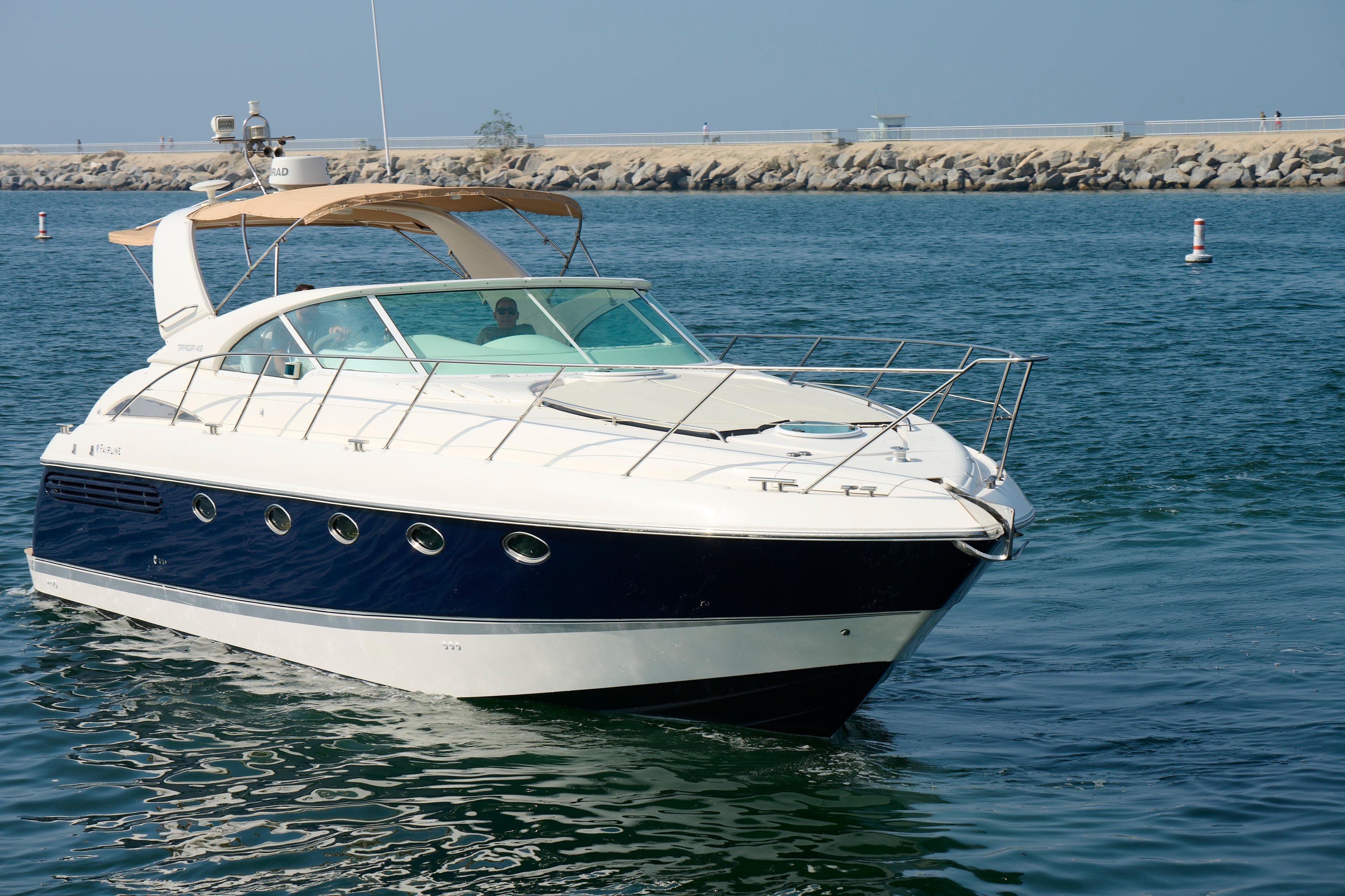 Luxury 2001 Fairline 43 yacht cruising in calm waters near a rocky shoreline.