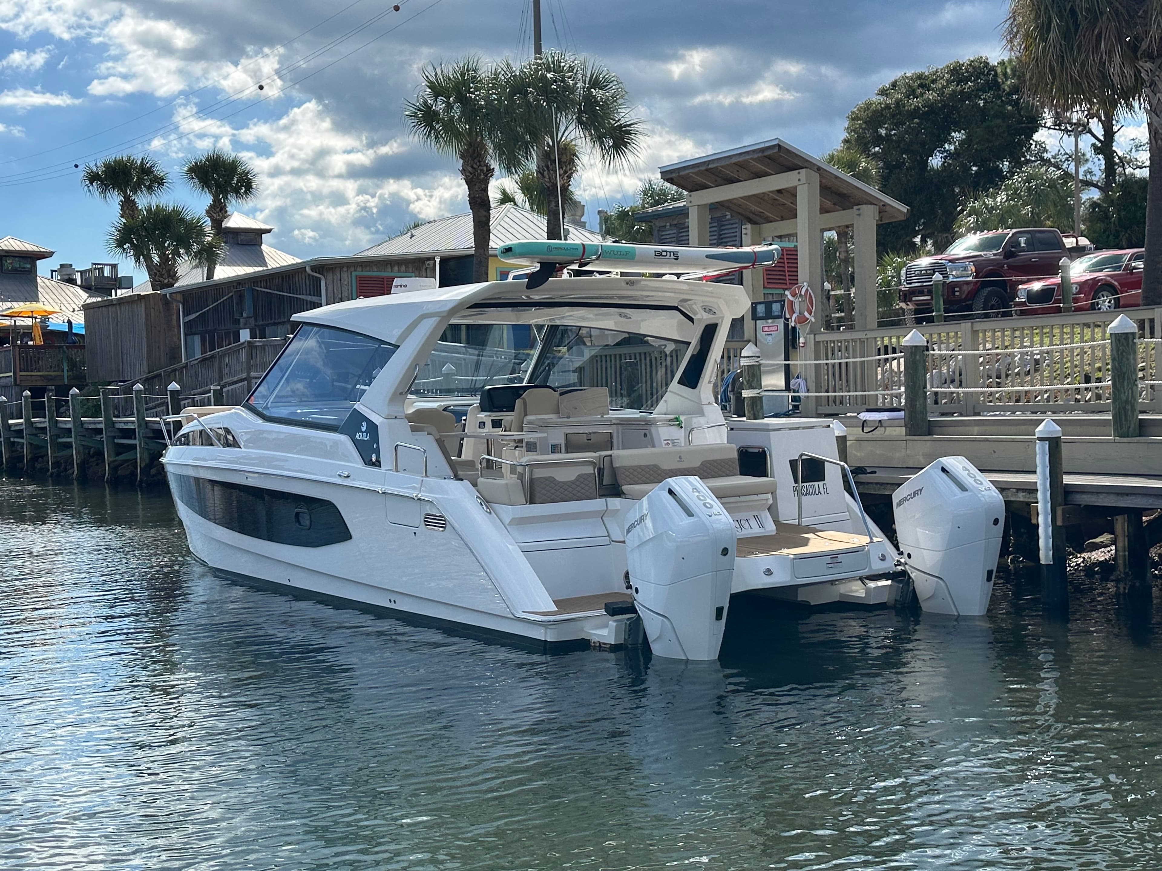 2025 Aquila 36 Sport boat docked by a wooden pier under a partly cloudy sky.