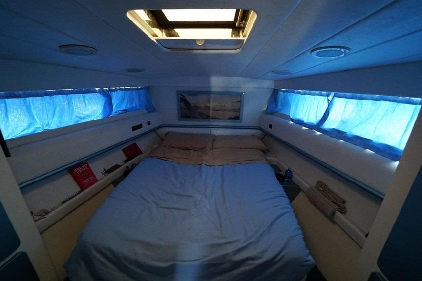 Cozy cabin interior of 1989 Baia 50 yacht with blue bedding and natural light.
