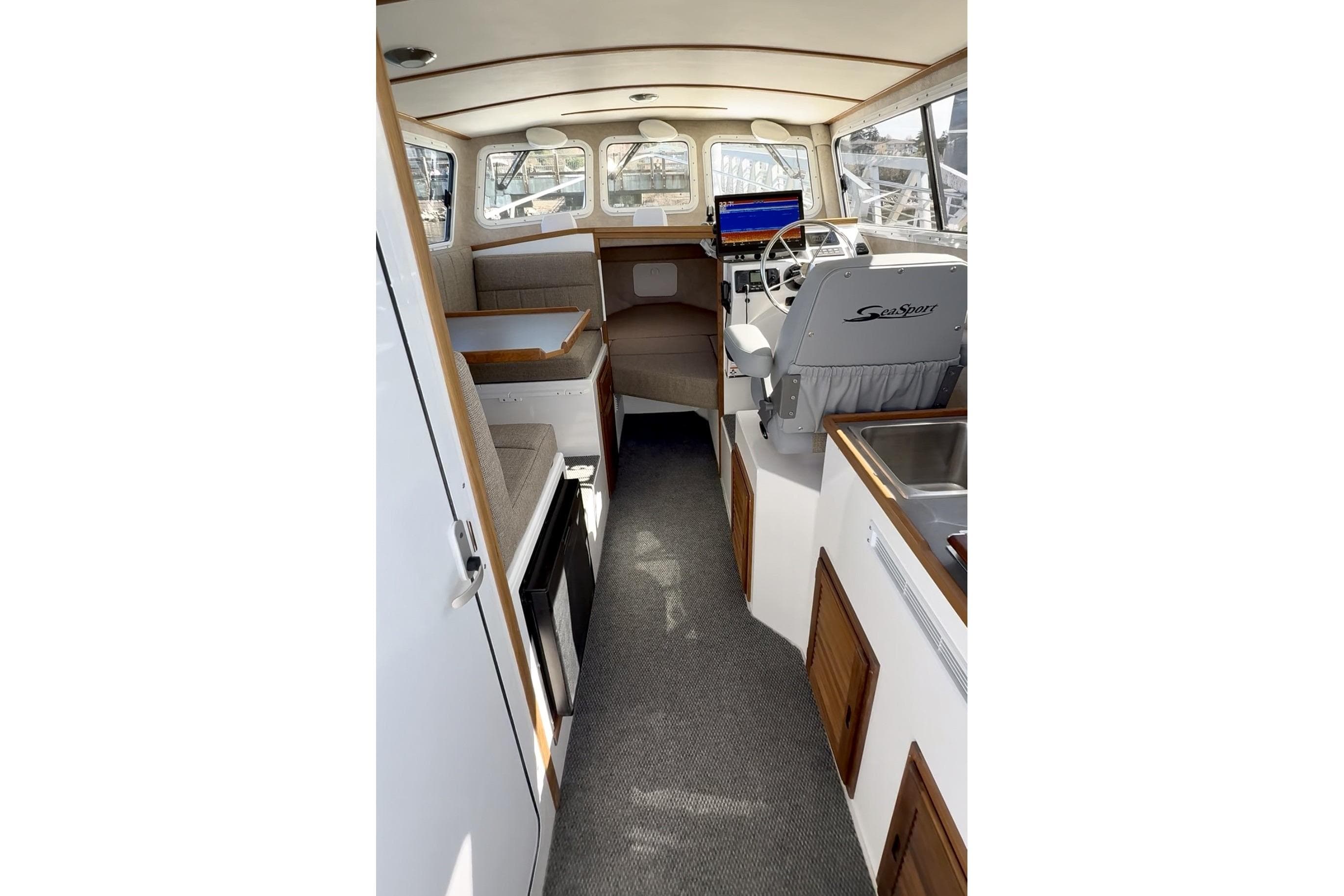 Interior of 2026 SeaSport Explorer 2400 boat, featuring helm, seating, and kitchenette.