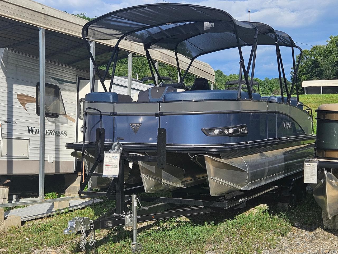2025 Tahoe Pontoon Cascade Cruise Rear Bench, blue, parked near RVs under a canopy.