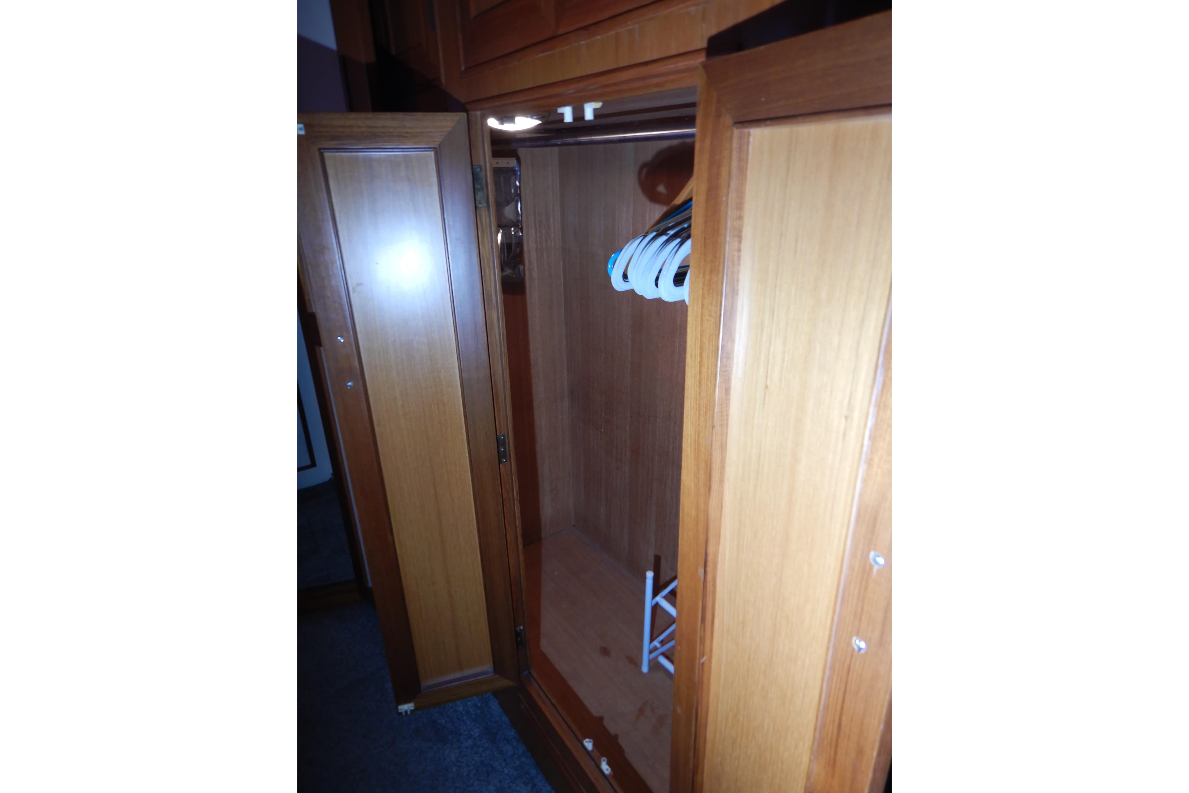 Wooden closet interior on 1988 Camargue 48 Cockpit Motor Yacht, featuring hangers and storage space.