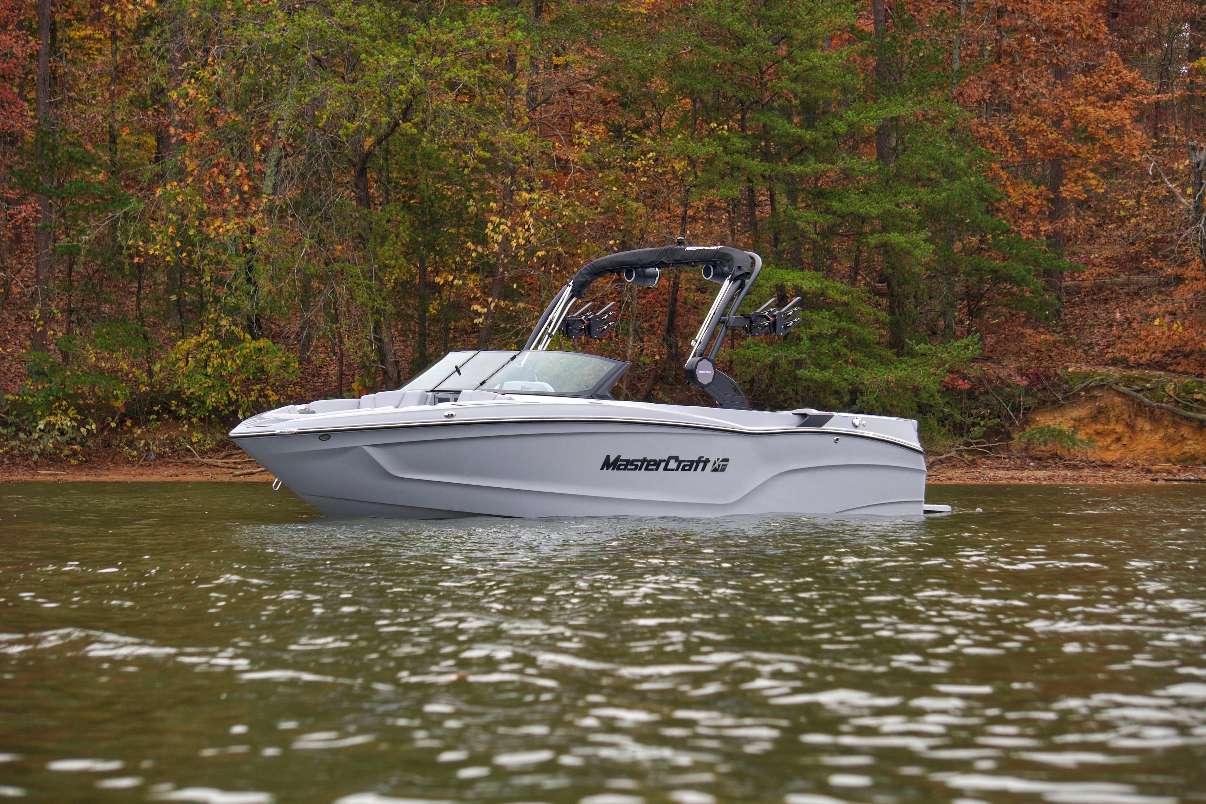 2025 MasterCraft XT23 boat on a lake with autumn trees in the background.