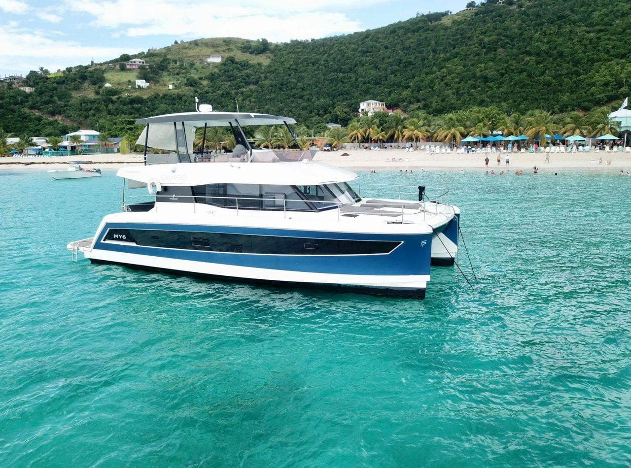 2021 Fountaine Pajot MY6 yacht anchored in turquoise waters near a tropical beach.