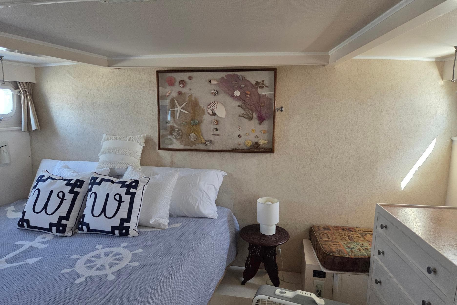 Cozy bedroom in 1966 Trumpy 55 yacht with nautical decor and seashell artwork.
