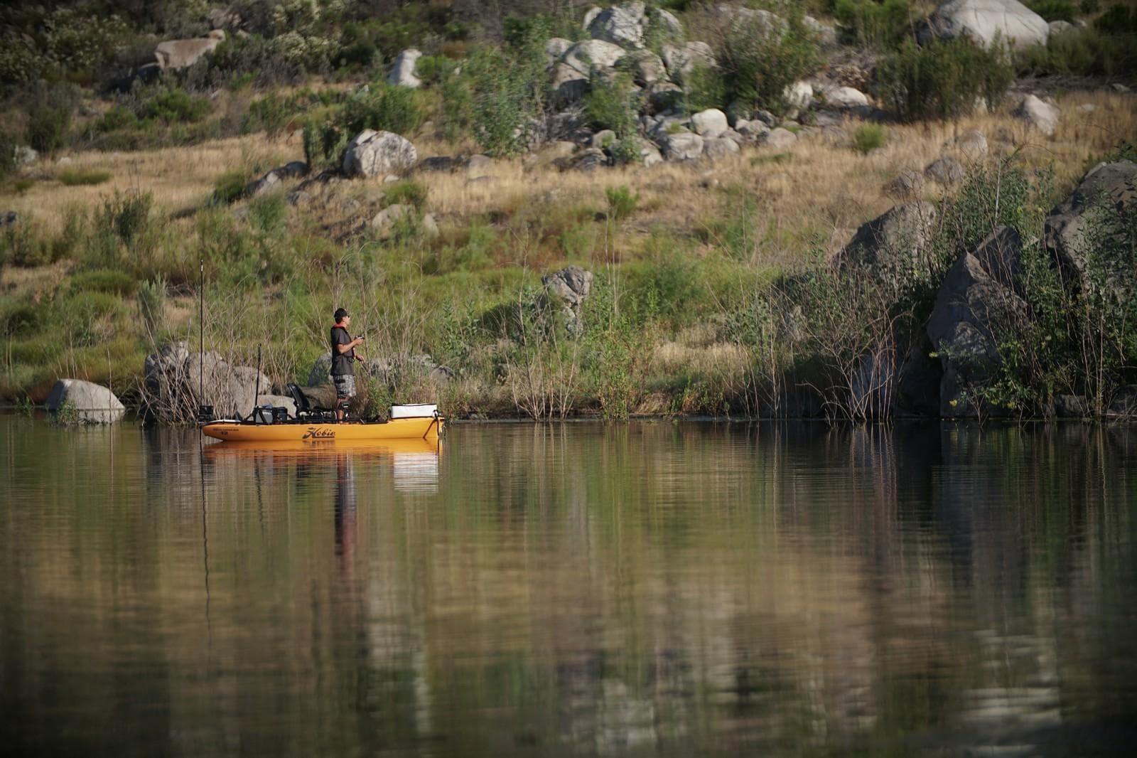 Man fishing on a 2023 Hobie Pro Angler 12 kayak in a serene lake.