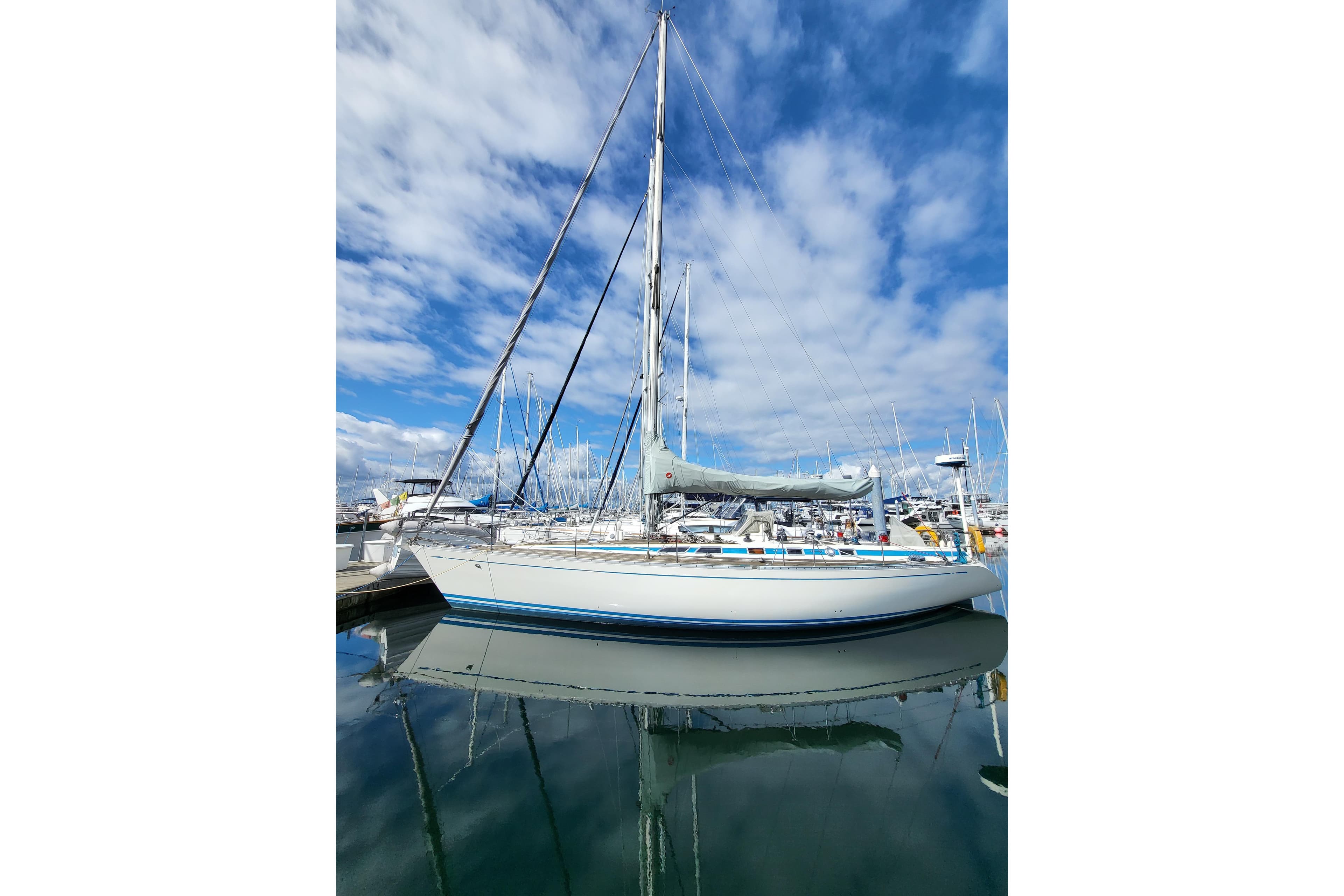 1985 Nautor Swan 46 sailboat docked, reflecting on calm water under a partly cloudy sky.
