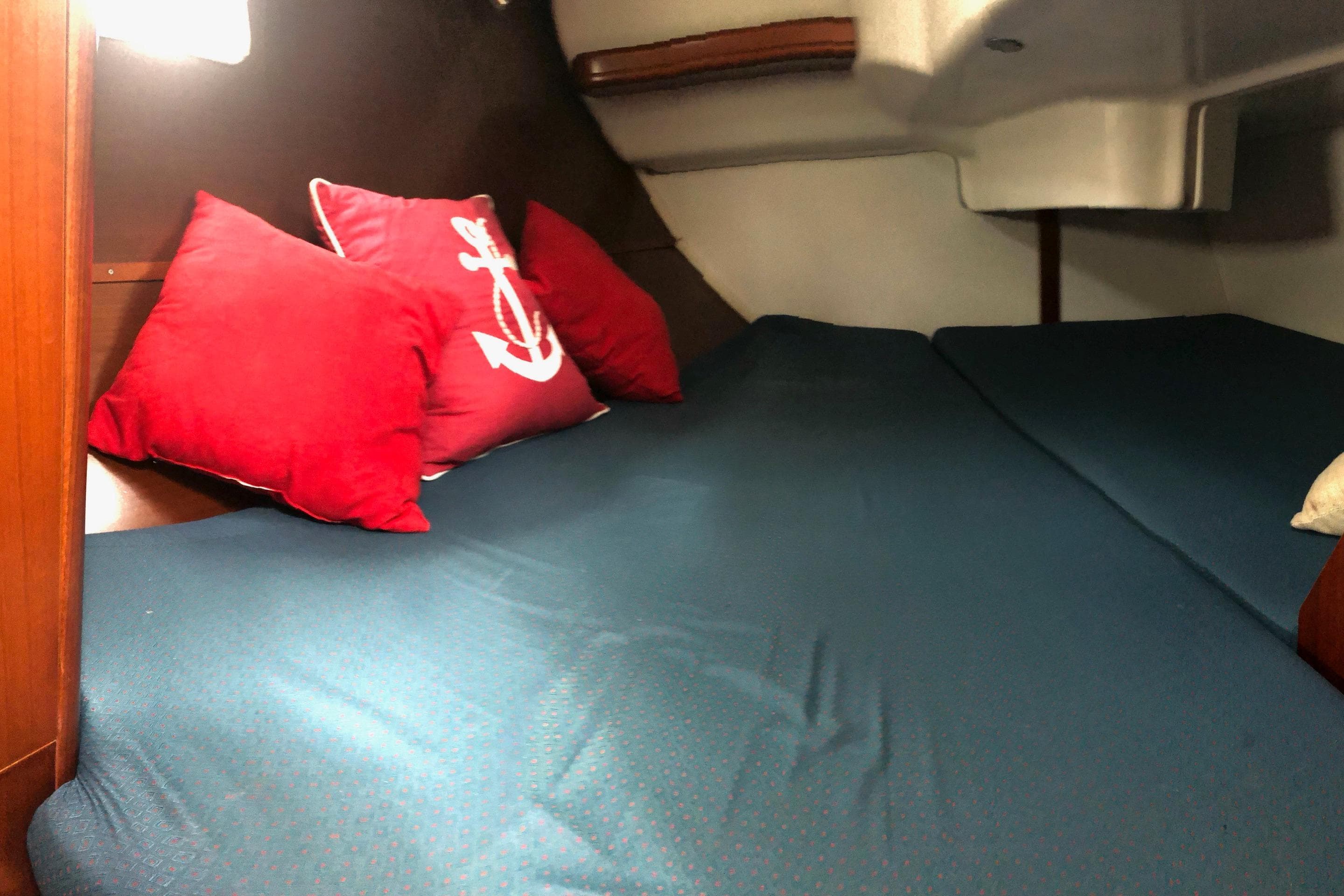 Cozy cabin interior of 2003 Beneteau 361 sailboat with red anchor-themed pillows.