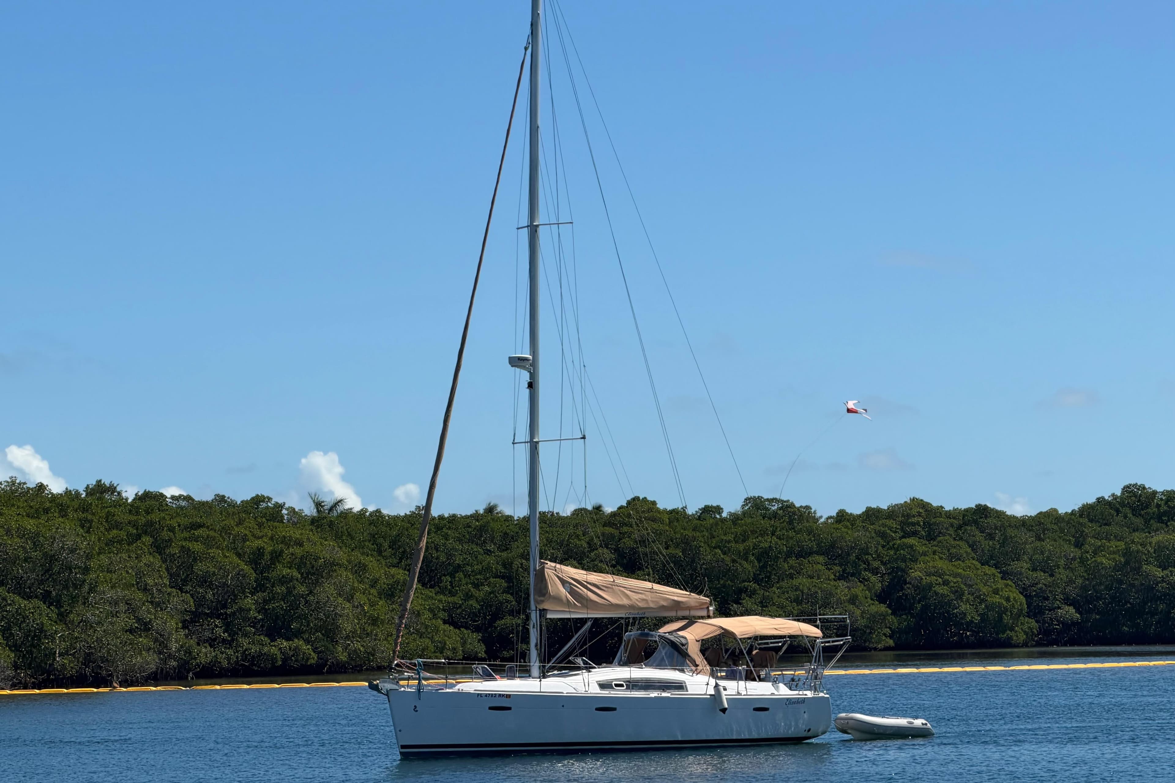 2008 Beneteau Oceanis 40 sailboat anchored near lush green shoreline under clear blue sky.