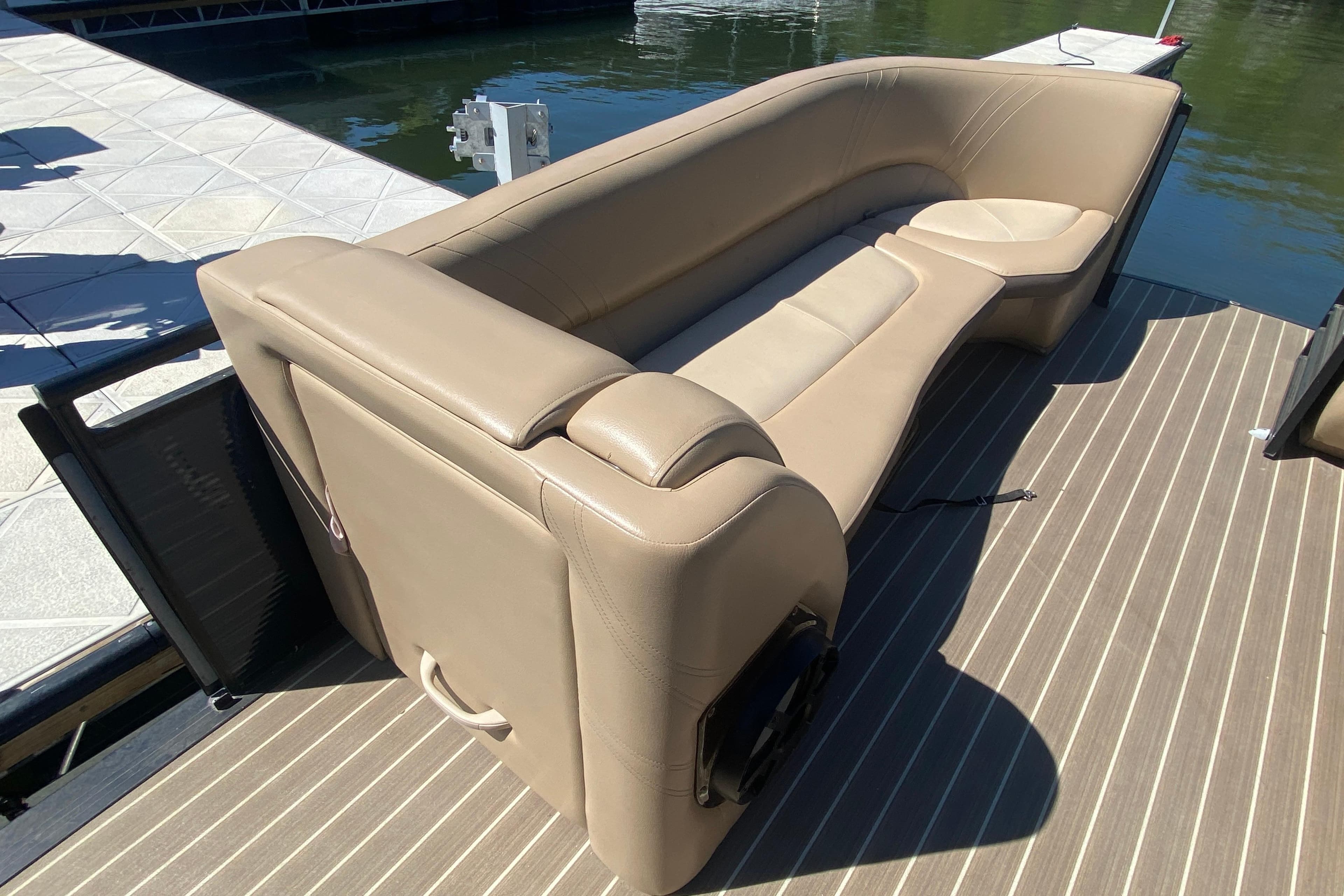 2018 Harris Solstice 240 boat with beige seating on a striped deck by the water.