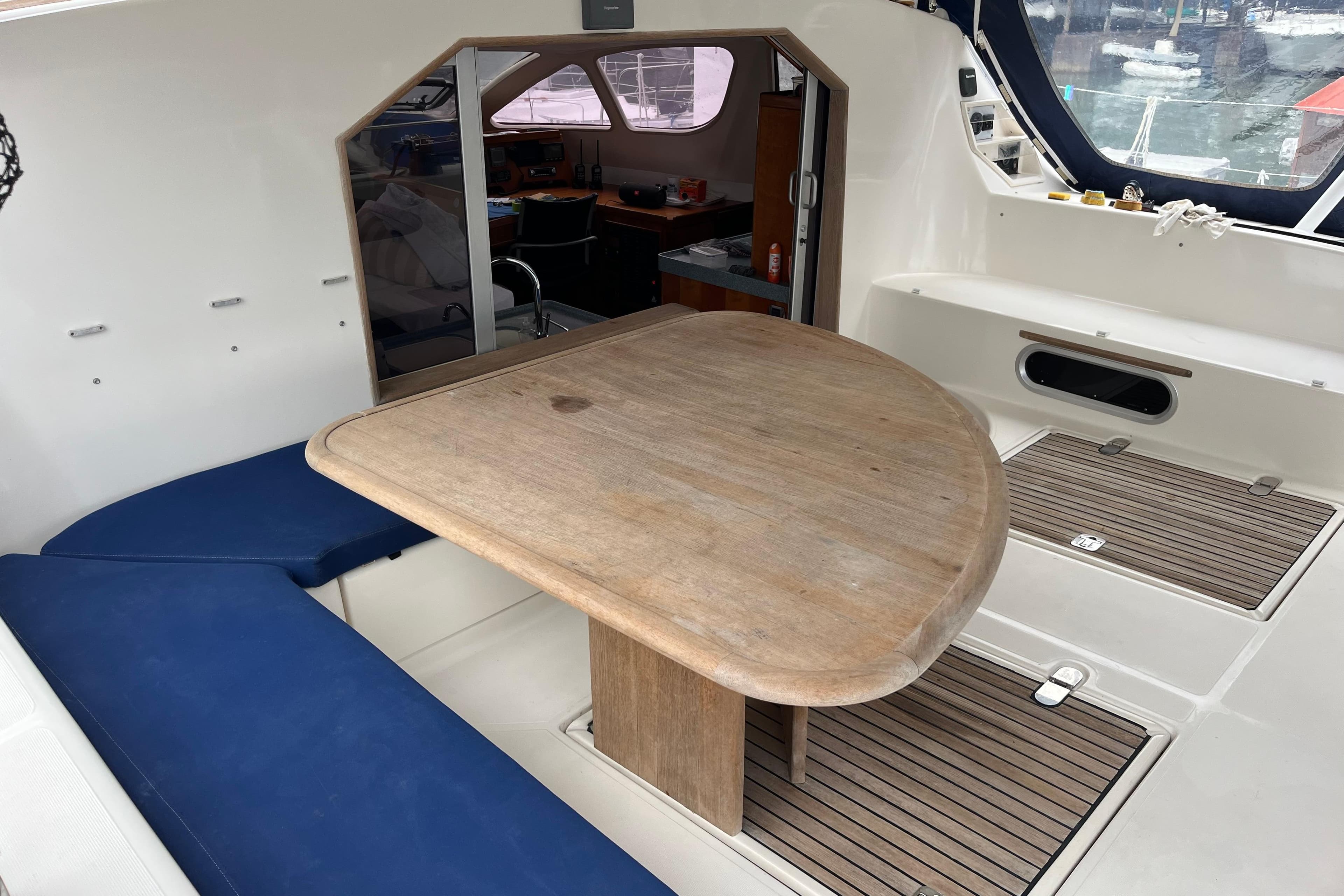Catana 471 Ocean Class 2004 yacht interior with wooden table and blue seating.