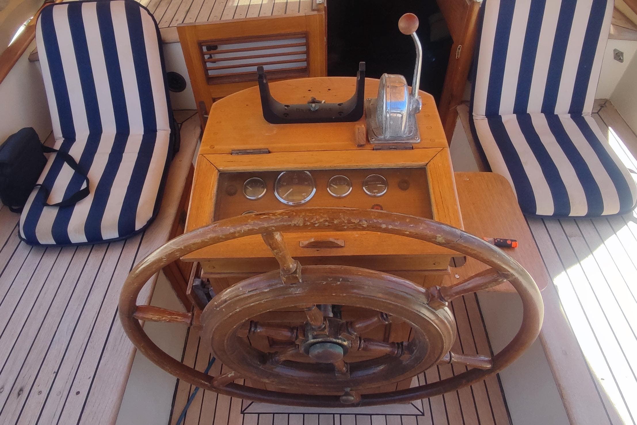 Vintage 1980 Formosa 51 yacht helm with wooden wheel and striped seating.