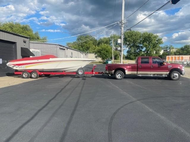 Red truck towing 1995 Fountain 27 Fever boat on trailer, parked on asphalt.
